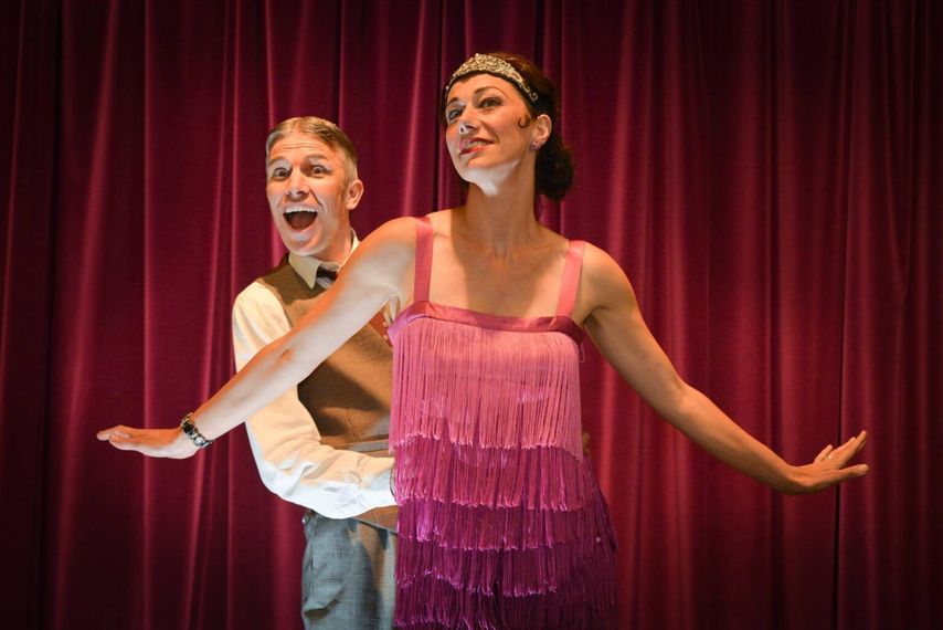 A man and a woman are dancing on a stage in front of a red curtain.