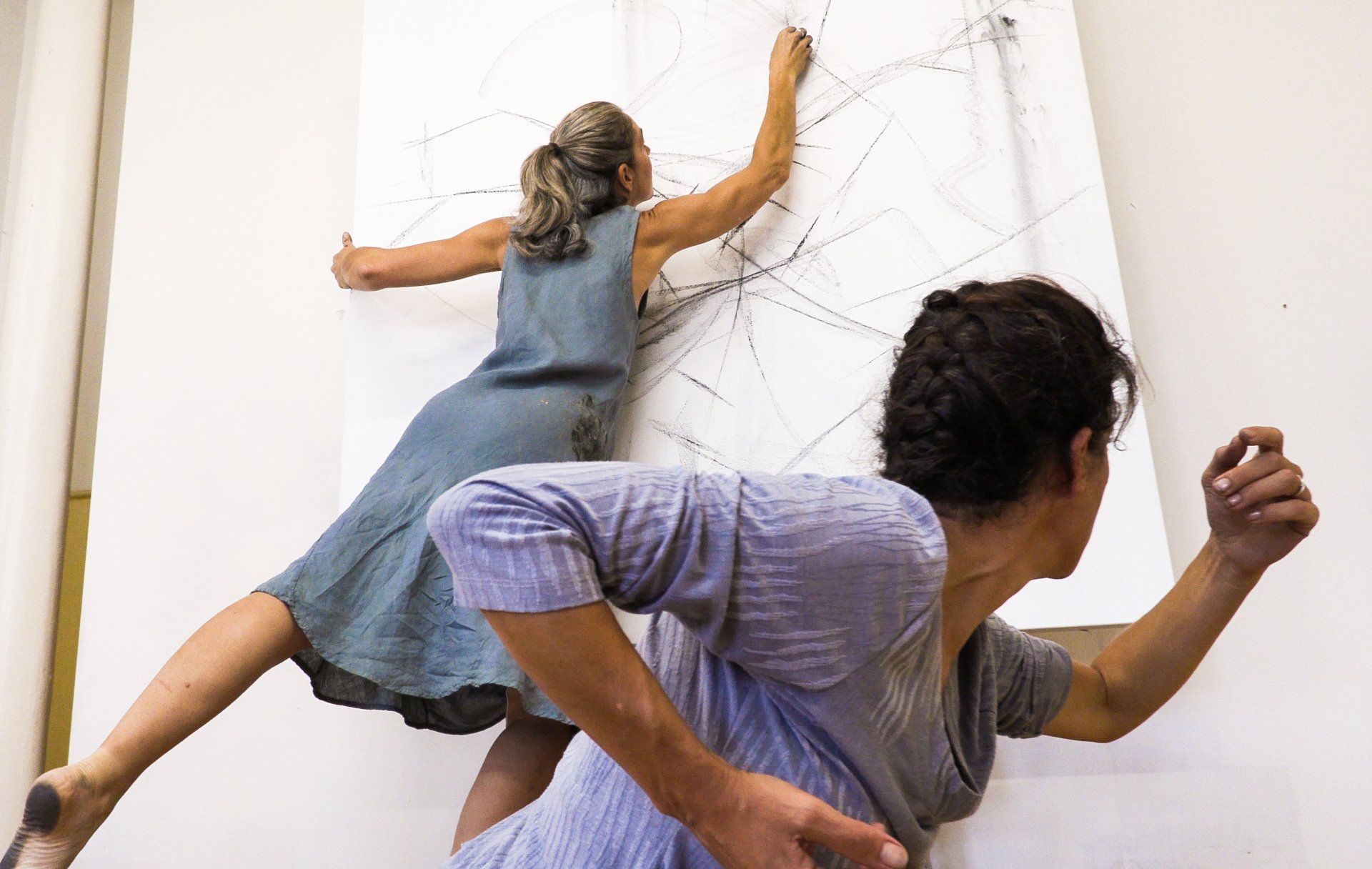 Two people in colorful dresses pose against a white wall with a drawn web pattern