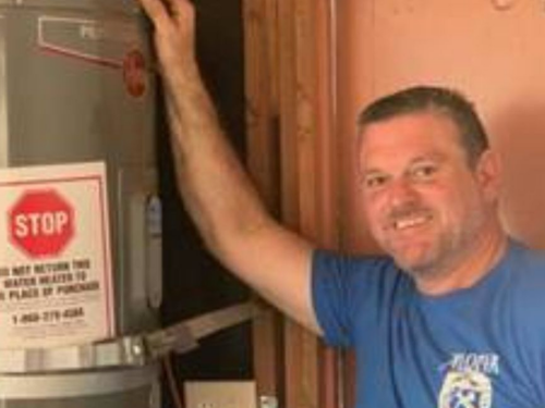 Man smiling beside a metal machine with a red STOP sign and warning label in an industrial setting