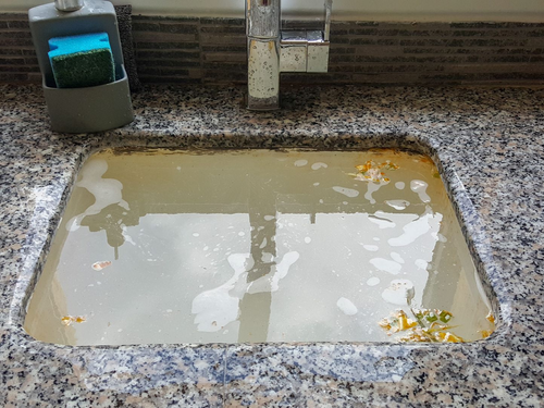 Dirty kitchen sink filled with cloudy water, with soap dispenser on the counter.