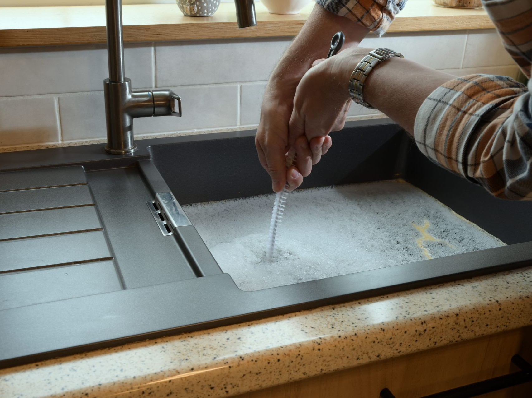 Hands washing under a kitchen faucet in a sink with water and suds.