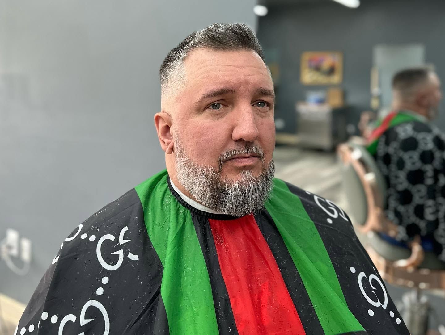 Man seated in a barber chair wearing a black-and-green barber cape, looking off to the side in a salon.