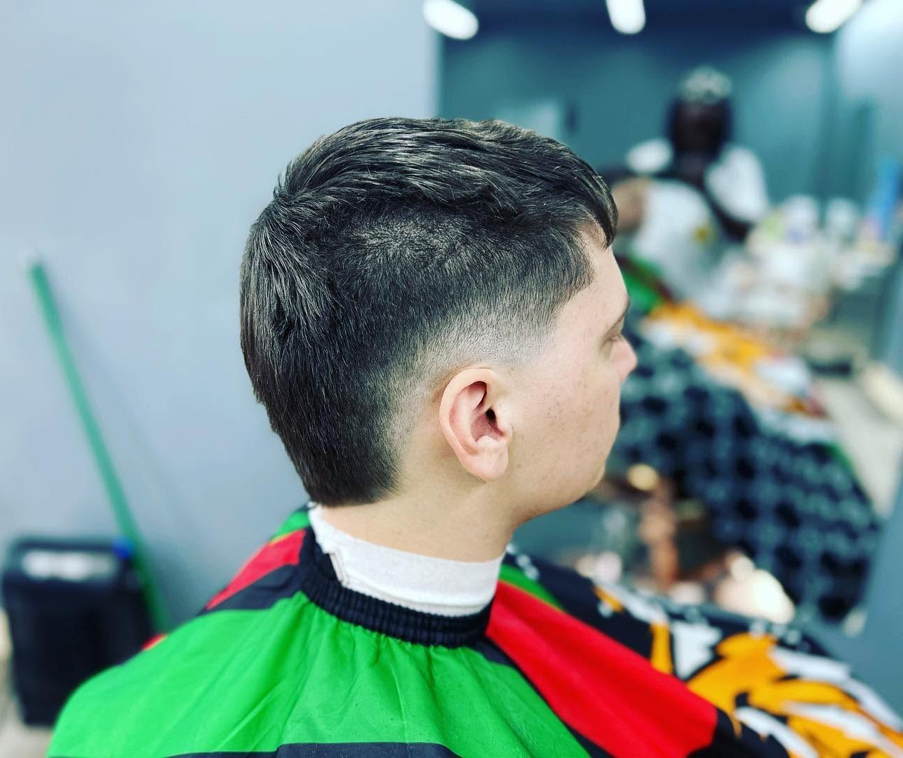 Person in a green barber cape with a fresh short fade haircut in a barbershop