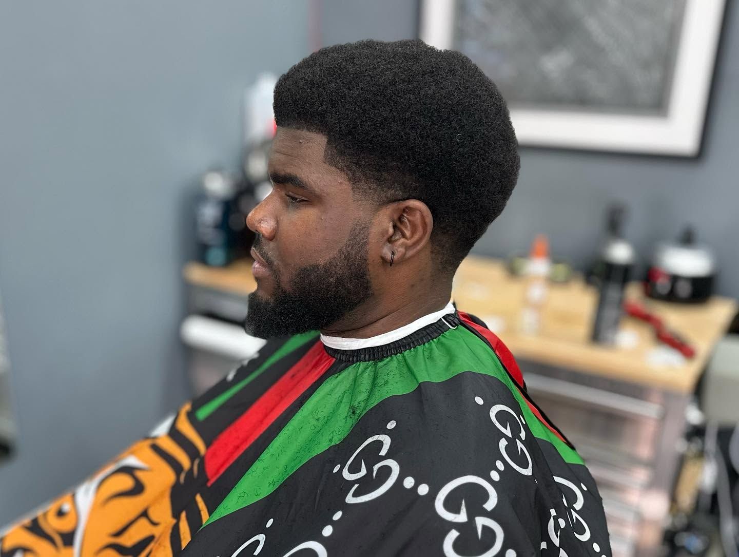 Side-profile portrait in a barbershop, with a man wearing a colorful barber cape and a neat beard.