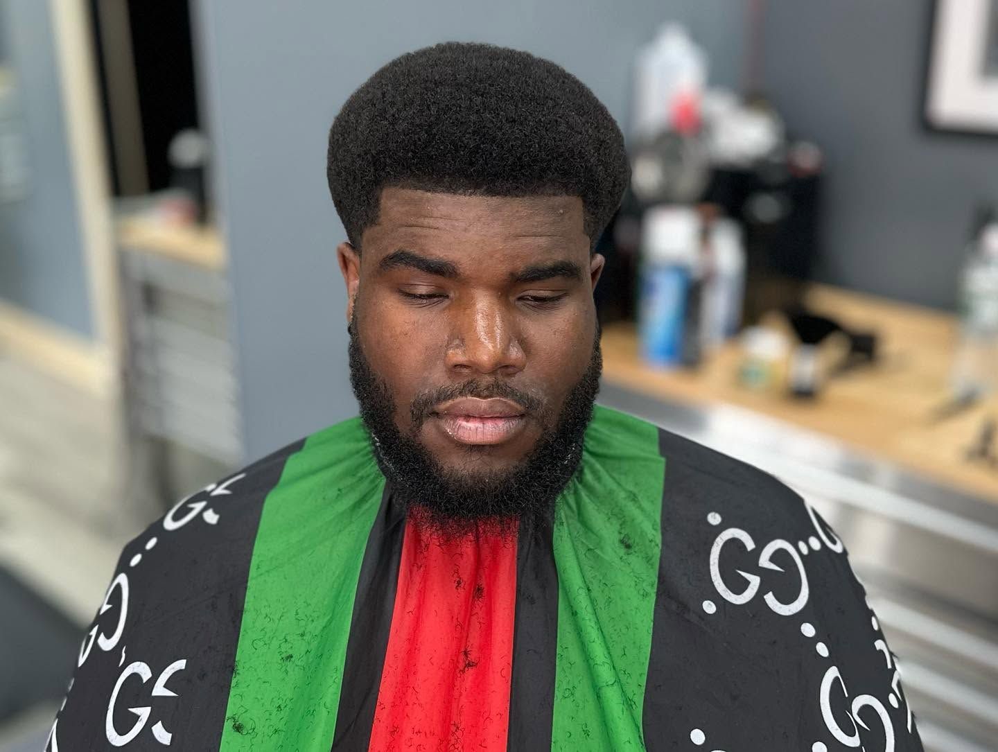 Person with eyes closed wearing a green, red, and black patterned garment in a salon setting