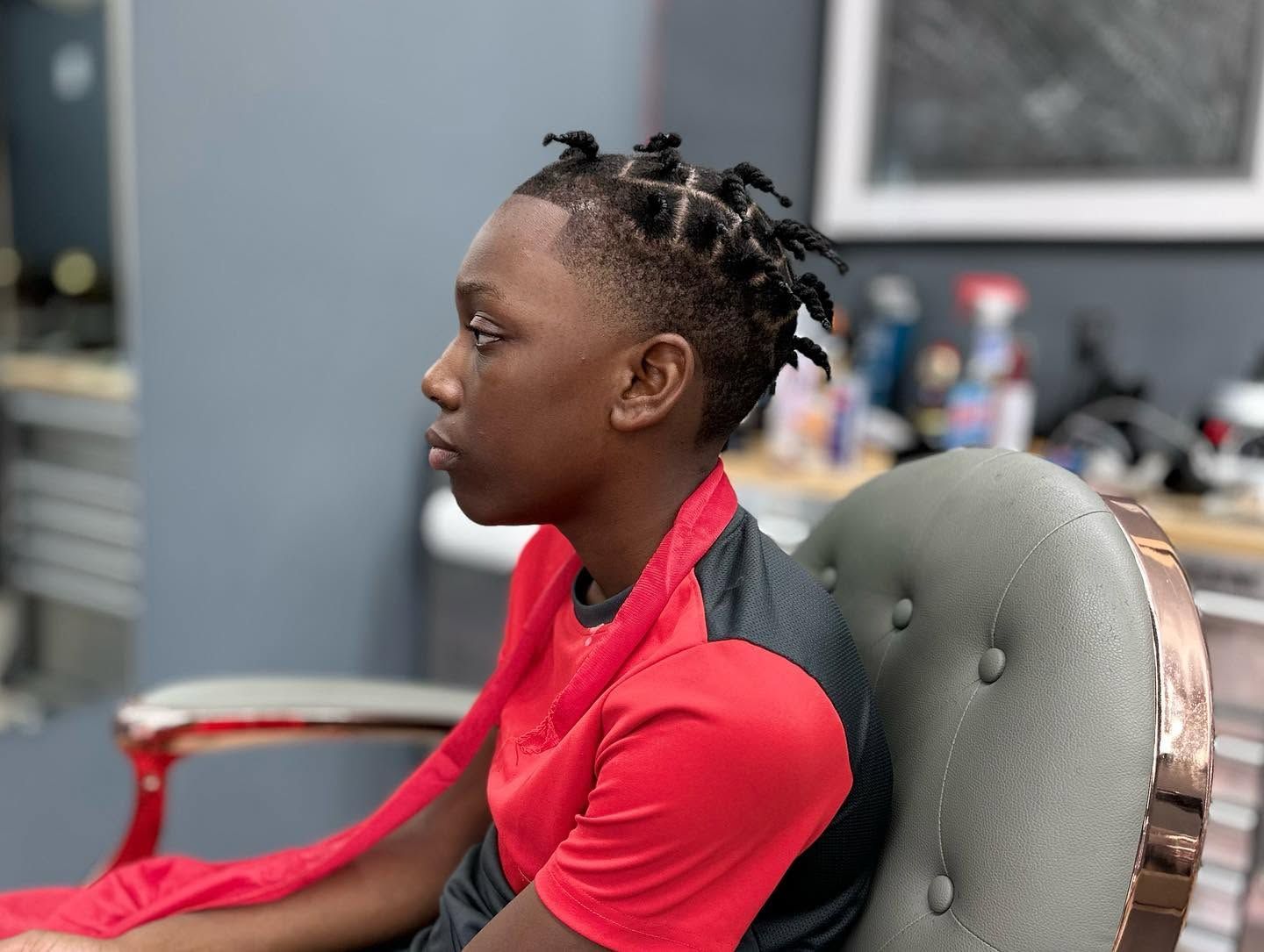 Person in a red top seated in profile, with braided hair, in a salon chair.