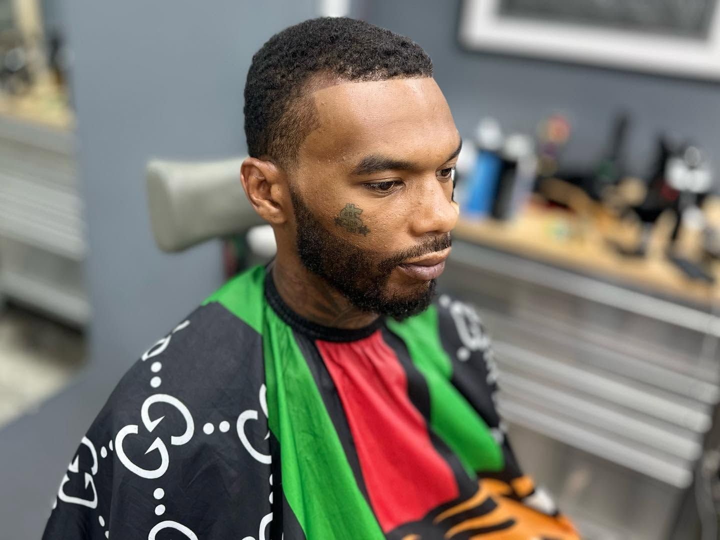 Man in a barber chair with a multicolored cape, looking down in a modern barbershop