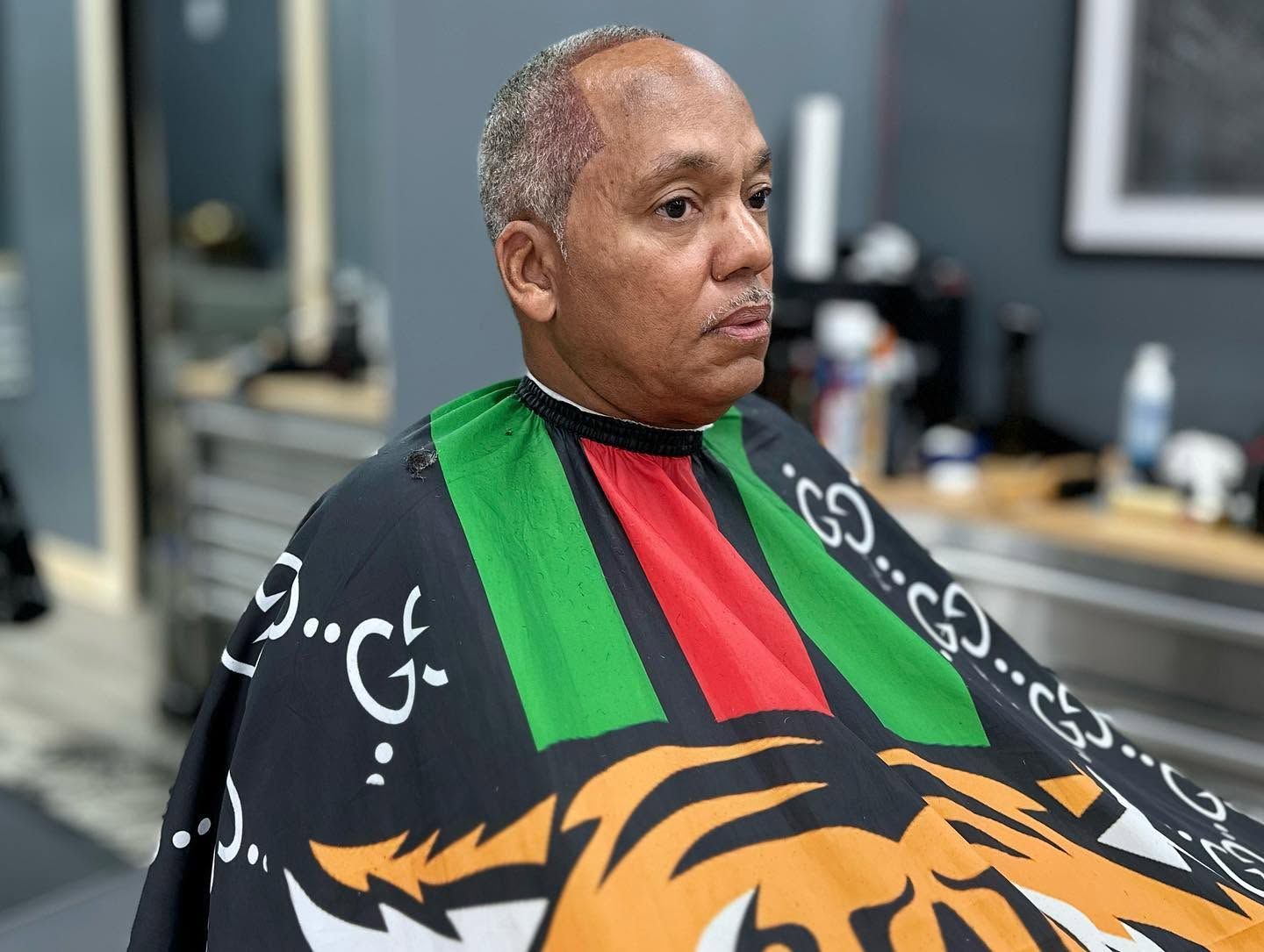 Man seated in a barber chair wearing a colorful cape with a tiger design