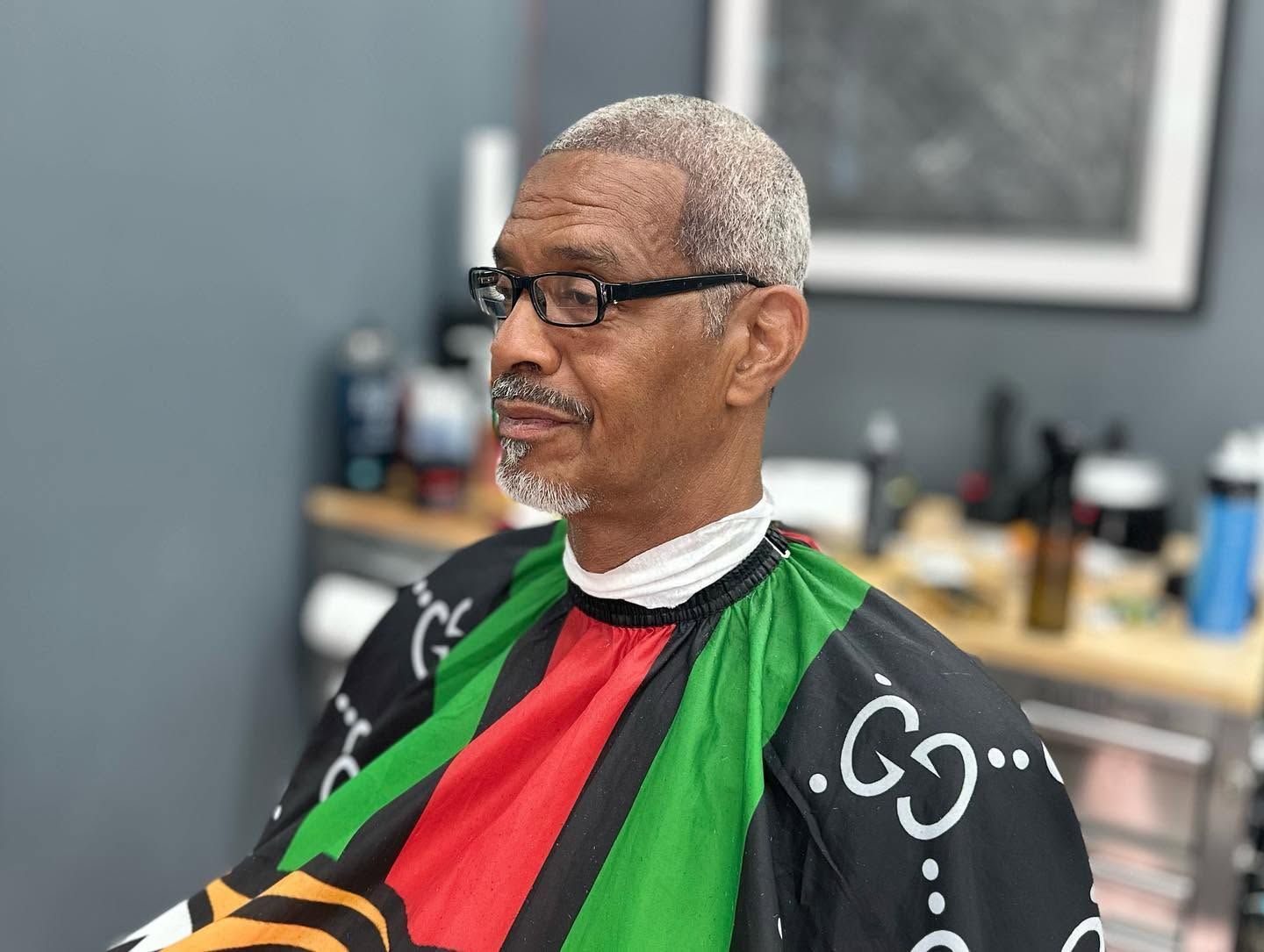 Man getting a haircut in a barber chair, wearing a red cape with green and black trim, in a salon.