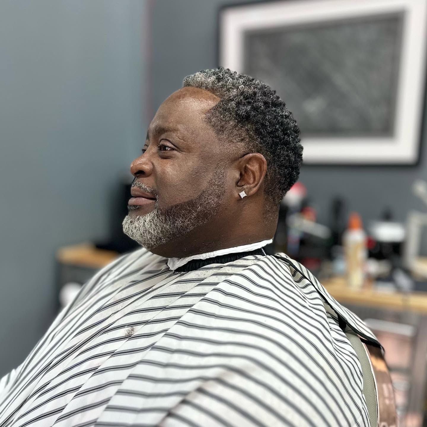 Profile view of a smiling man in a striped barber cape at a barbershop