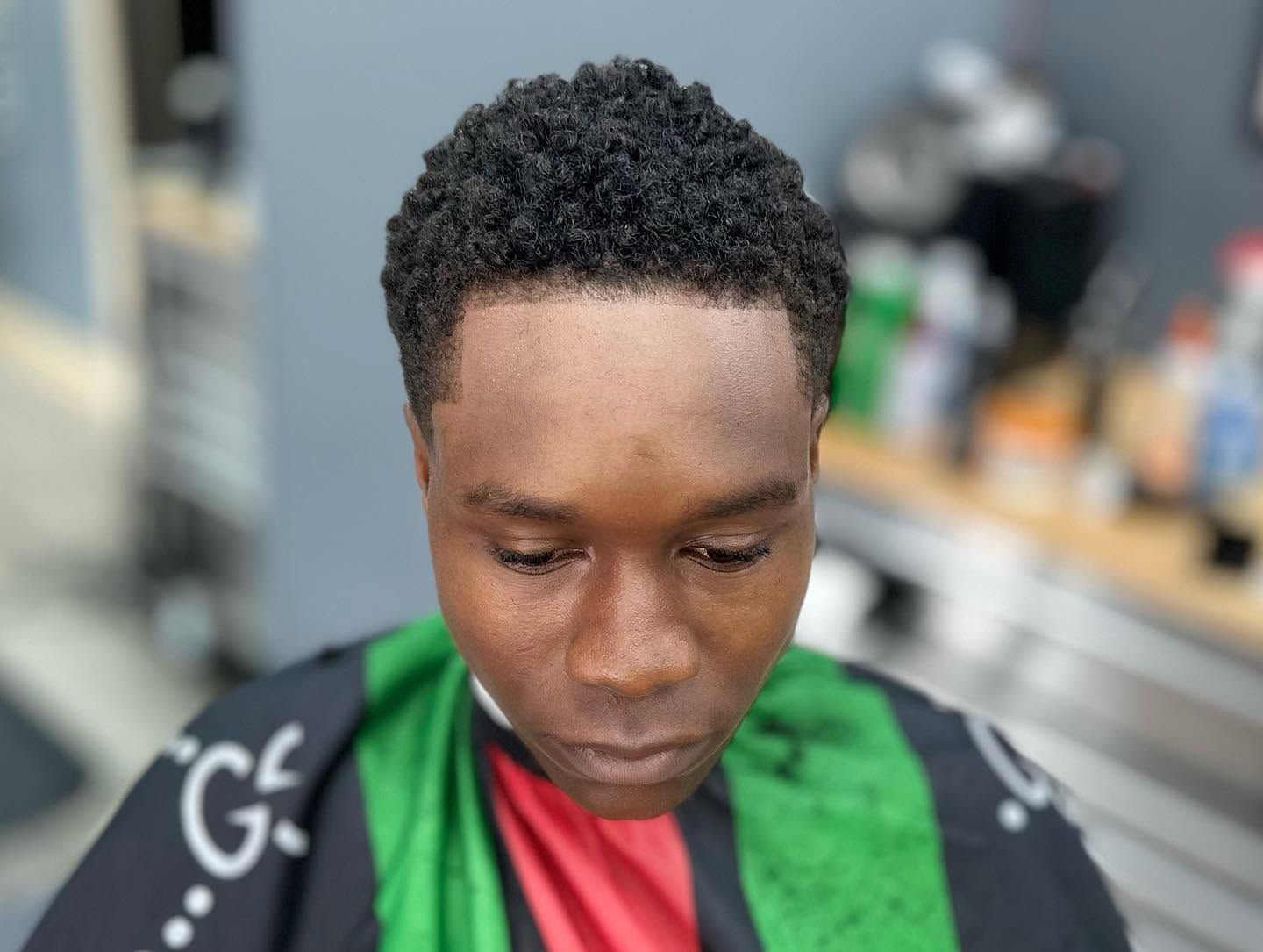 Person looking down in a barber chair, wearing a black cape with green and red stripes.