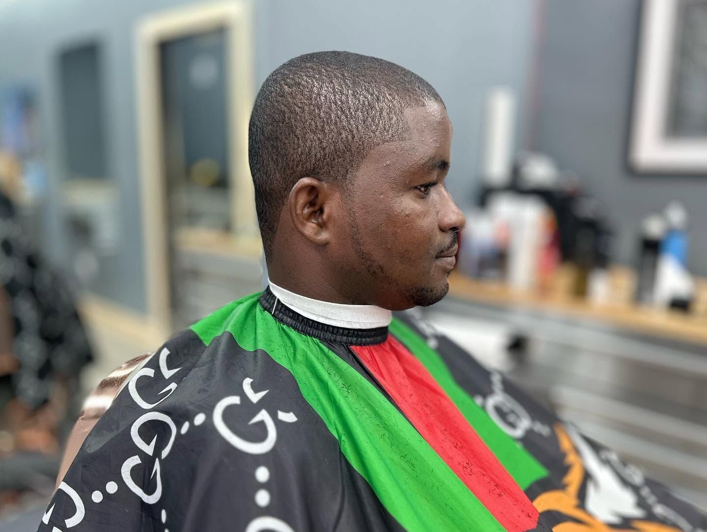 Person in a barber chair wearing a black, green, and red cape, shown in profile in a salon