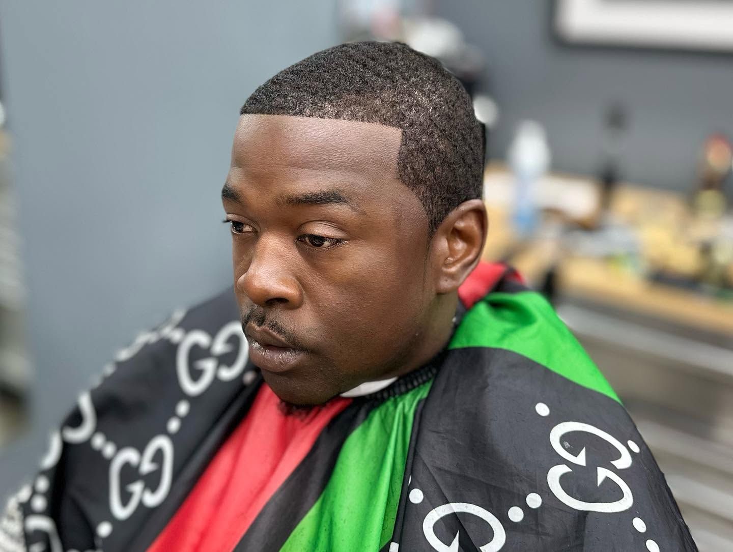 Man in a barber chair wearing a black, green, and red cape, looking to the side