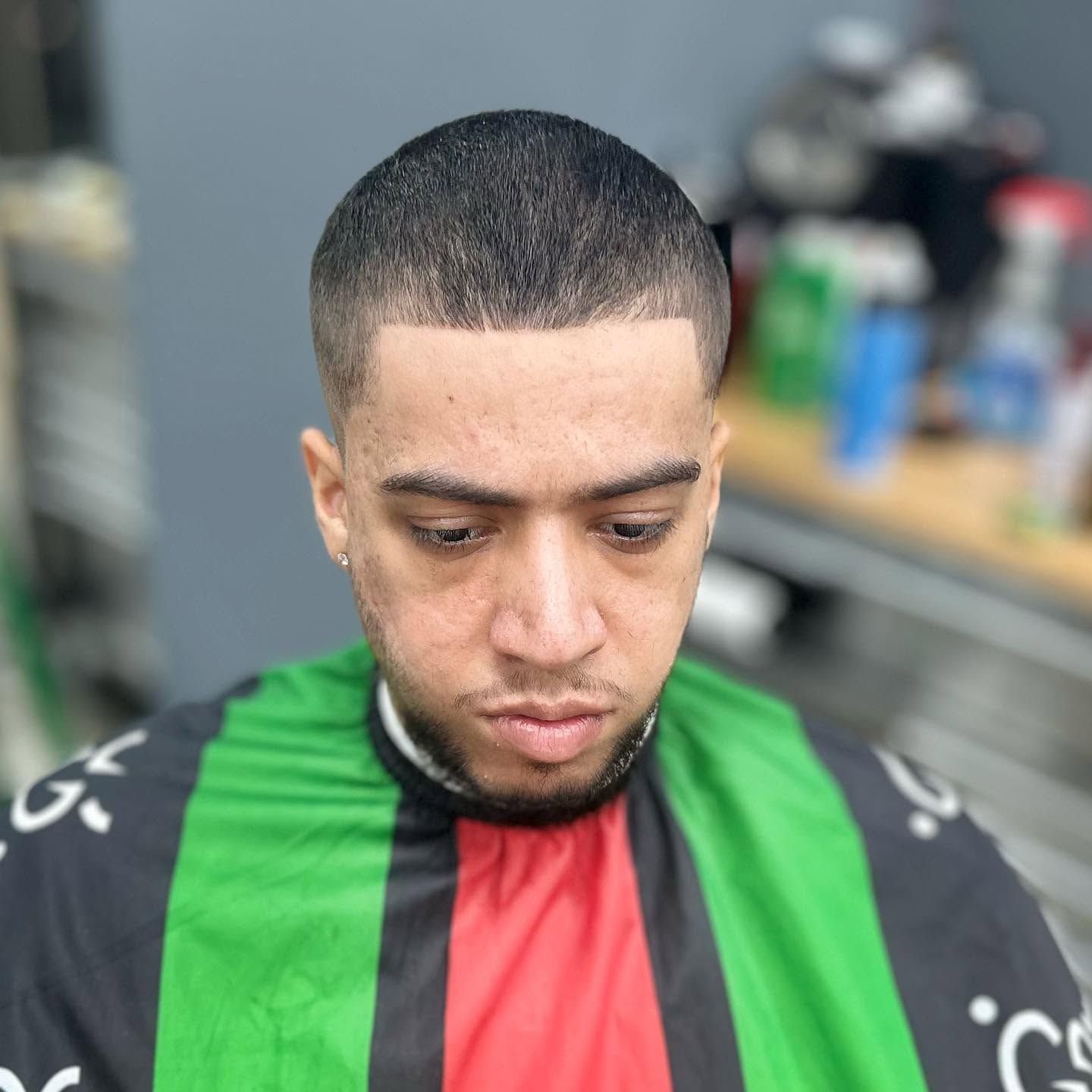 Man in a green and red barber cape looking down in a barbershop chair