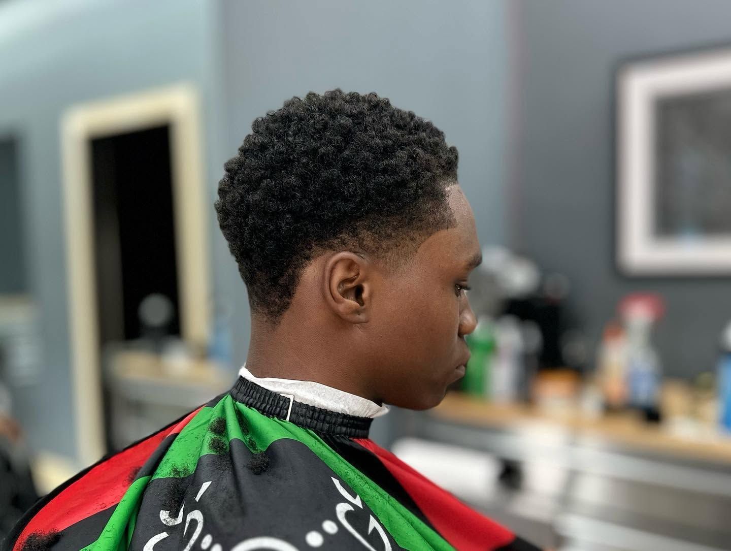 Person getting a haircut in a barbershop, wearing a green and red cape, side profile view