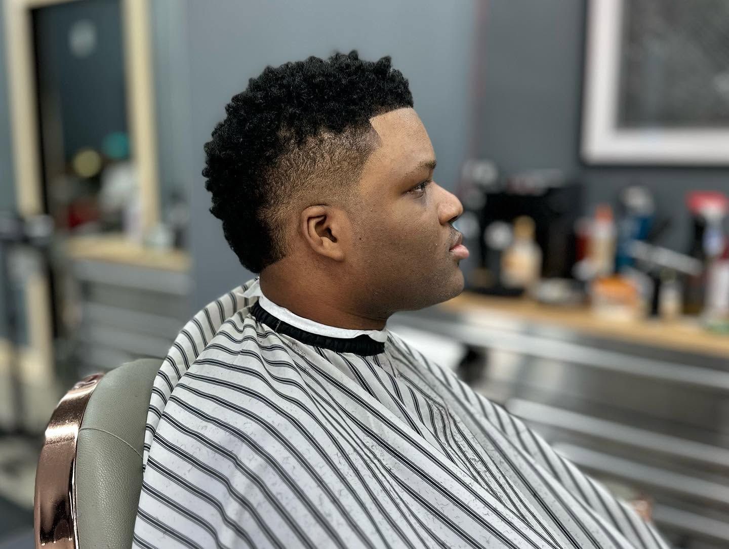 Man in a striped barber cape sitting in a barbershop chair, side profile, preparing for a haircut