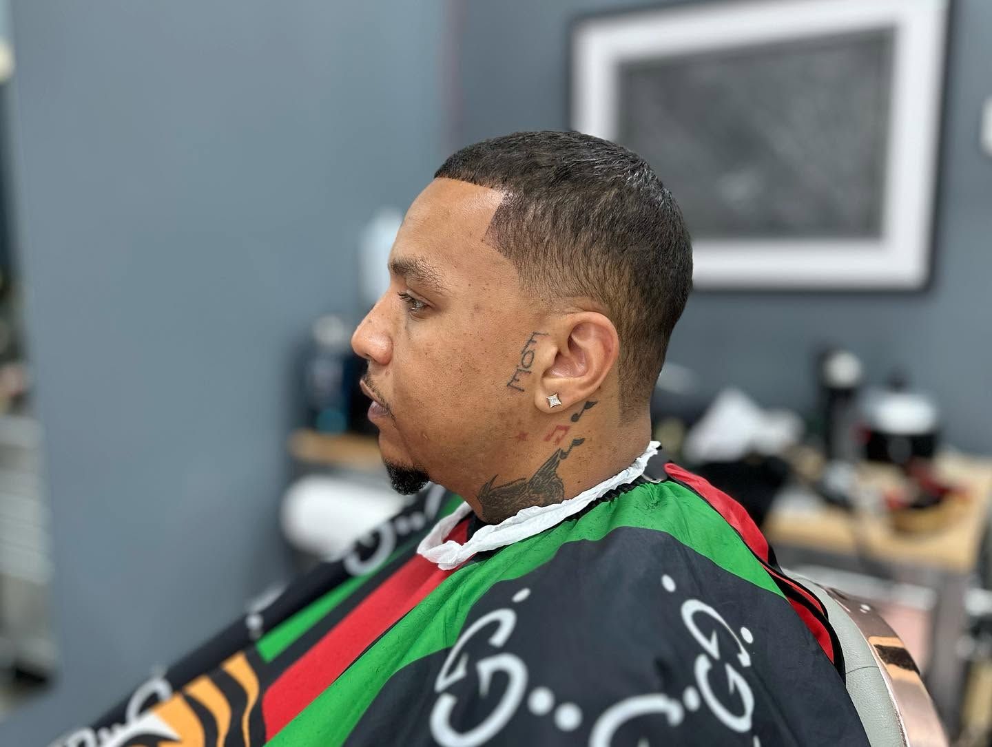 Man in a black, green, and red barber cape sitting in a barbershop chair, side profile.