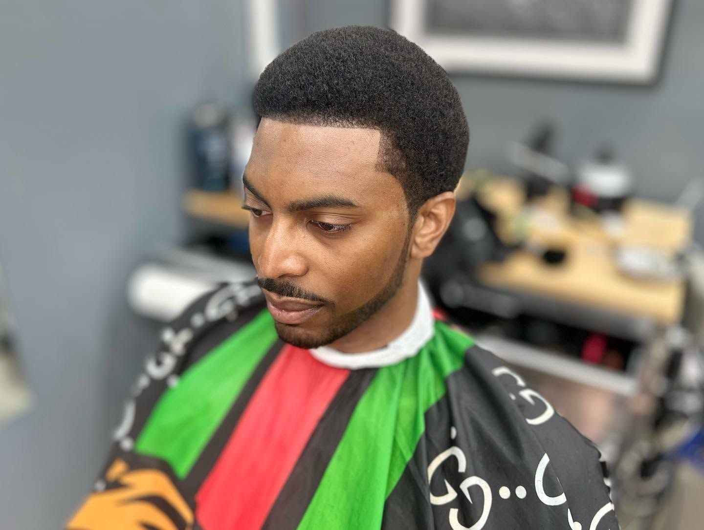 Person seated in a barbershop chair wearing a green, red, and black haircut cape