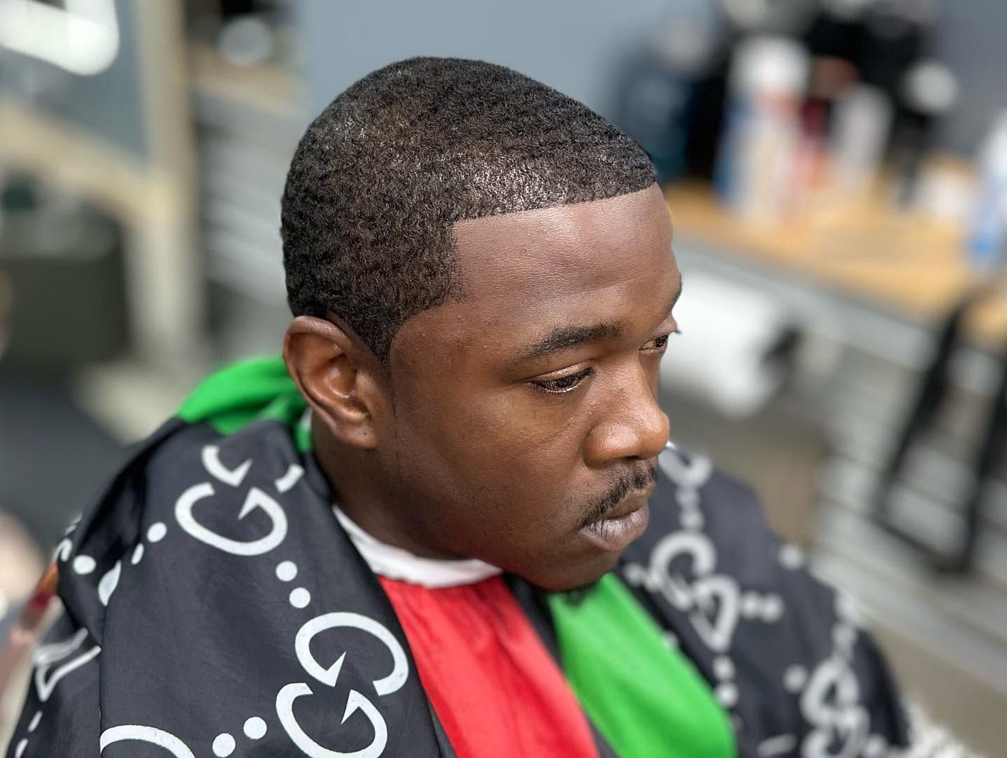 Close-up of a man wearing a black Gucci-patterned cape with green and red stripes, looking to the side.