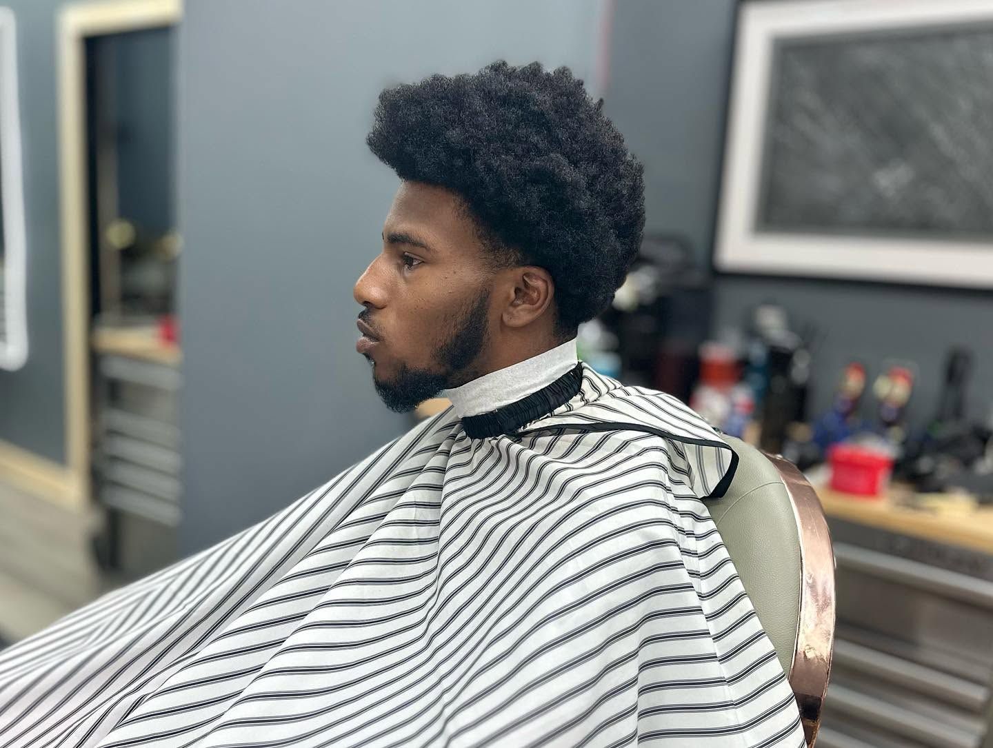 Person seated in a barber chair, wearing a striped cape during a haircut.