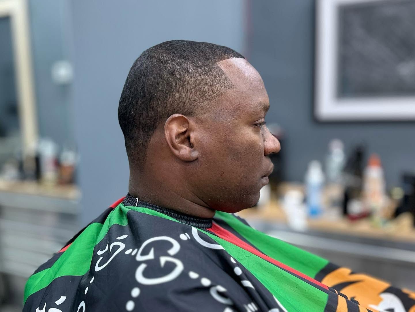 Man sitting in a barber chair, wearing a green-and-black cape during a haircut.