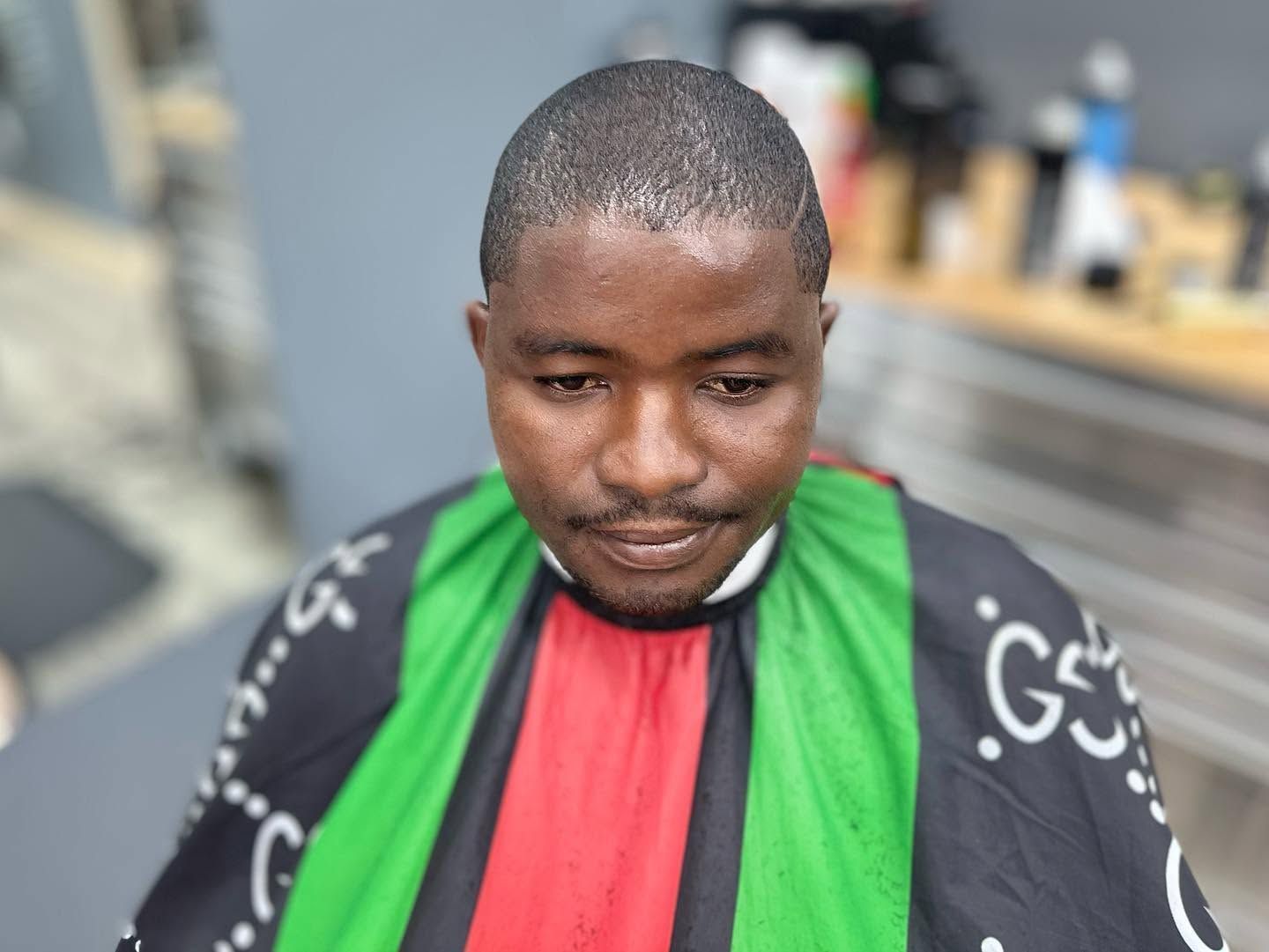 Person wearing a green, red, and black striped cape, looking down outdoors.