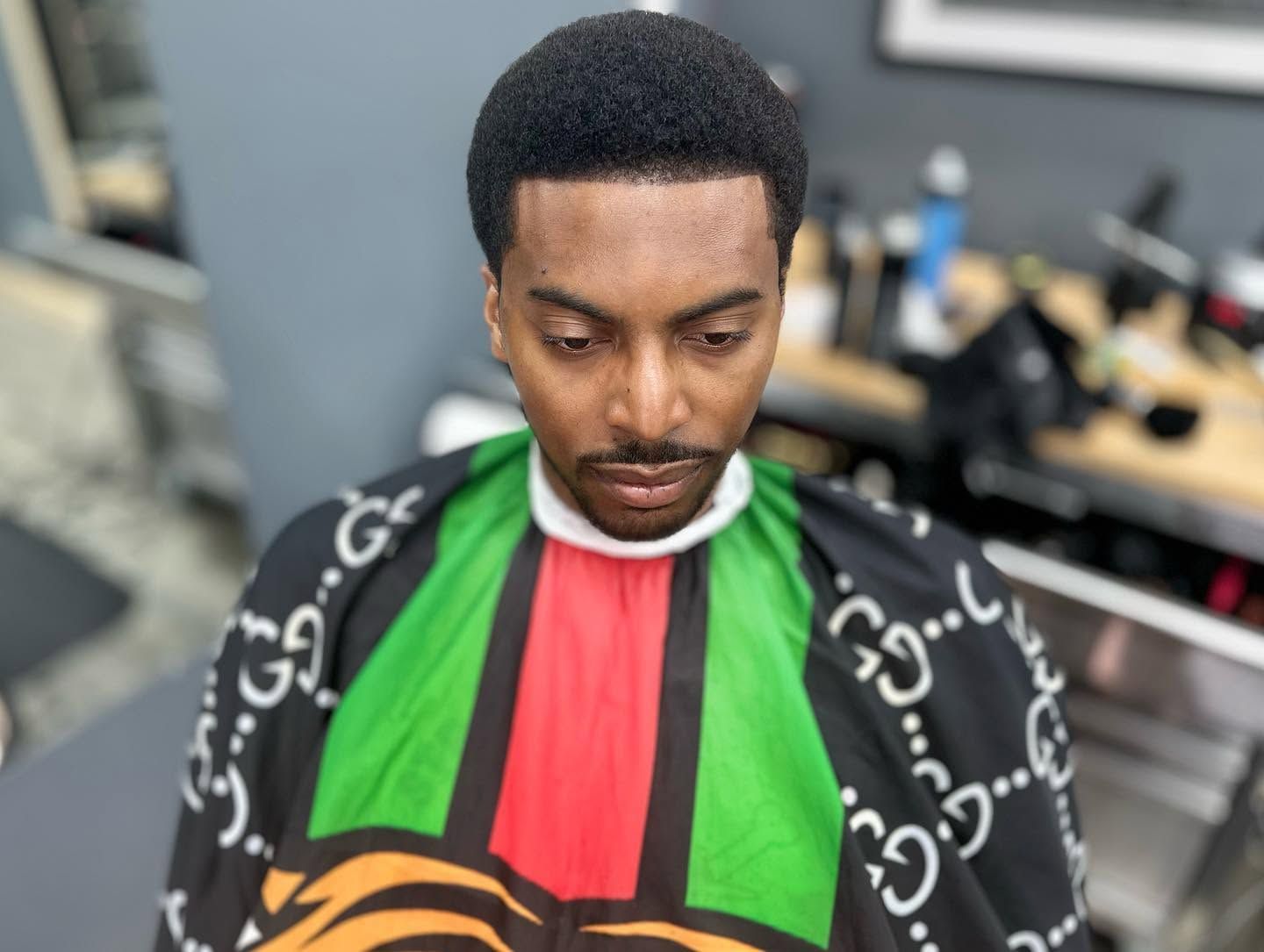 Man getting a haircut in a barber chair, wearing a black cape with green and red panels.