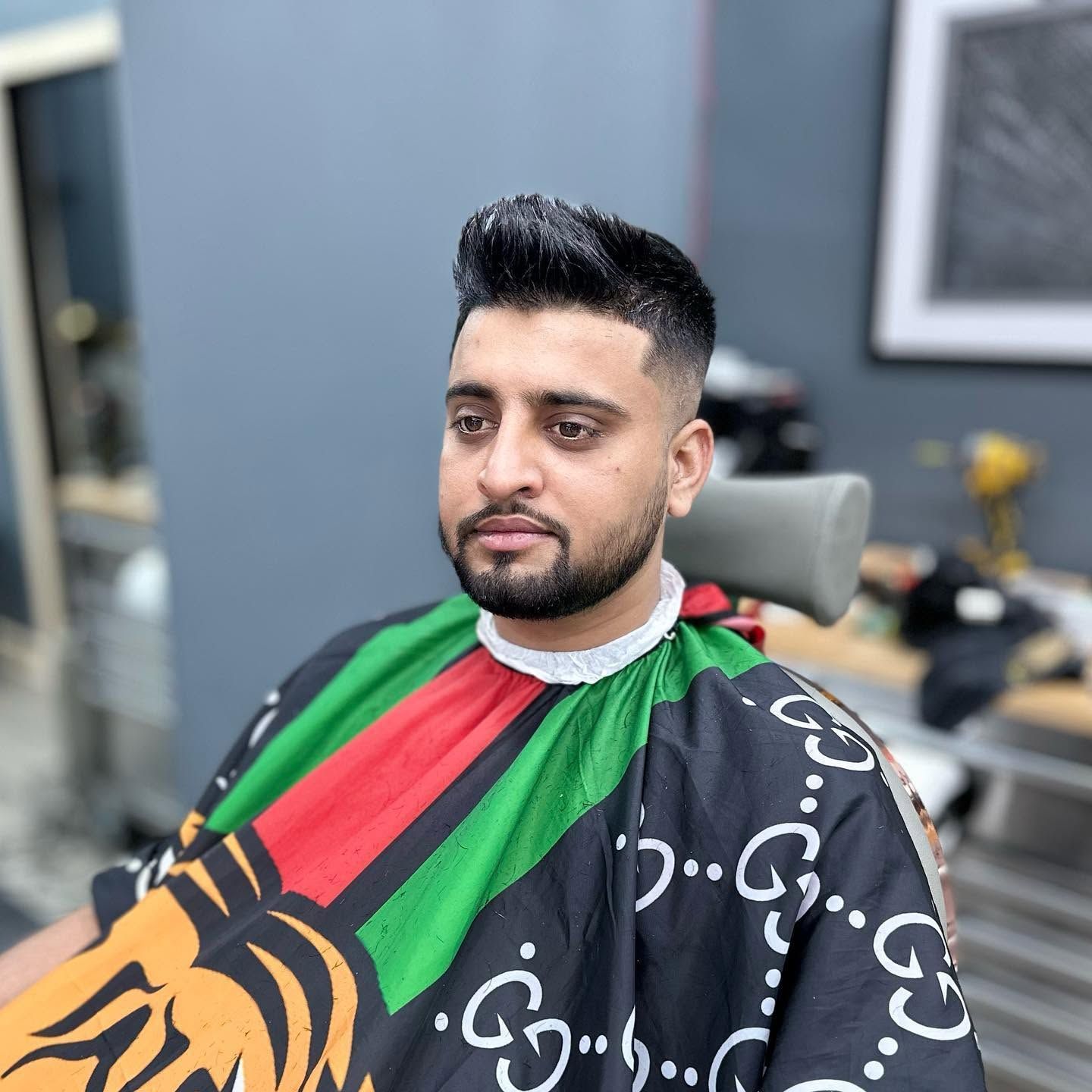 Man seated in a barber chair wearing a colorful Gucci cape, in a modern barbershop.