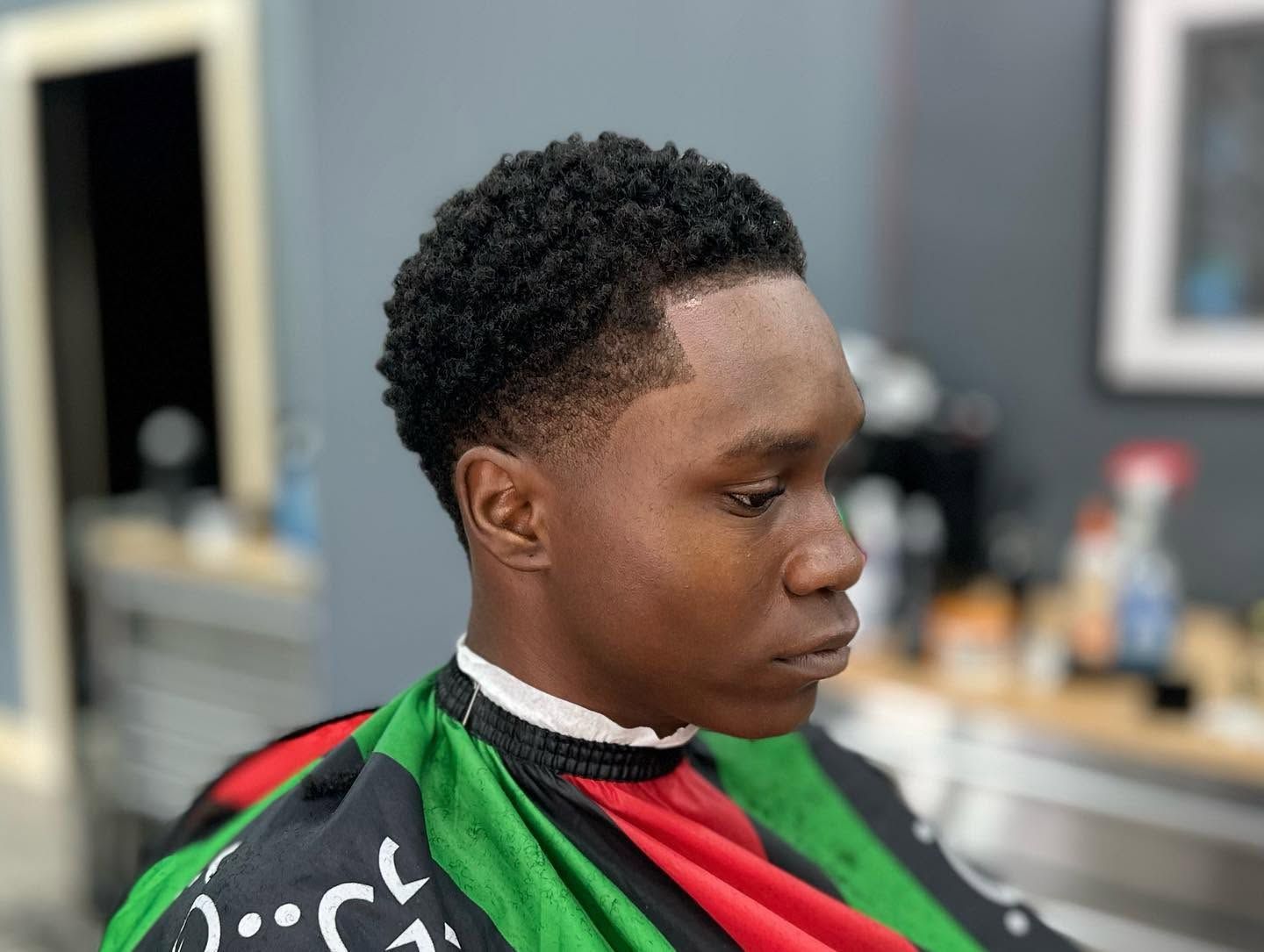 Person getting a haircut in a barbershop, wearing a red and green barber cape.