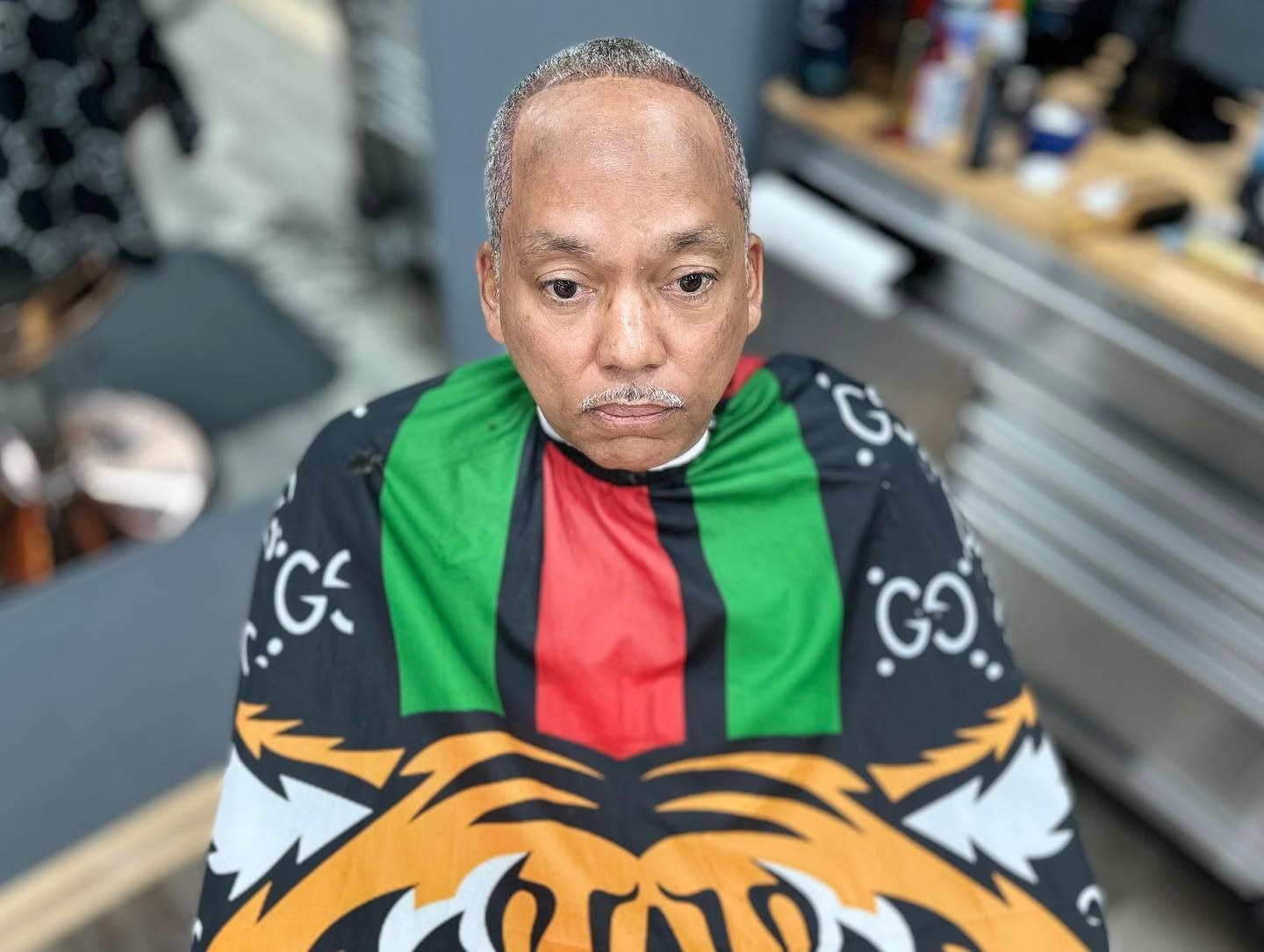 Person wearing a red and green striped cape with a tiger design, seated indoors and looking downward