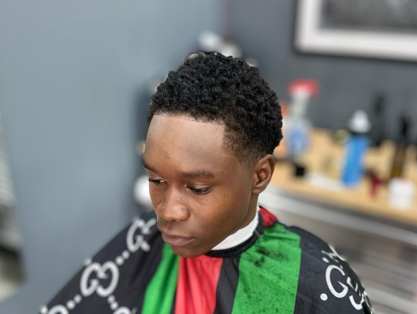 Person wearing a black, red, and green barber cape, looking down in a salon chair.