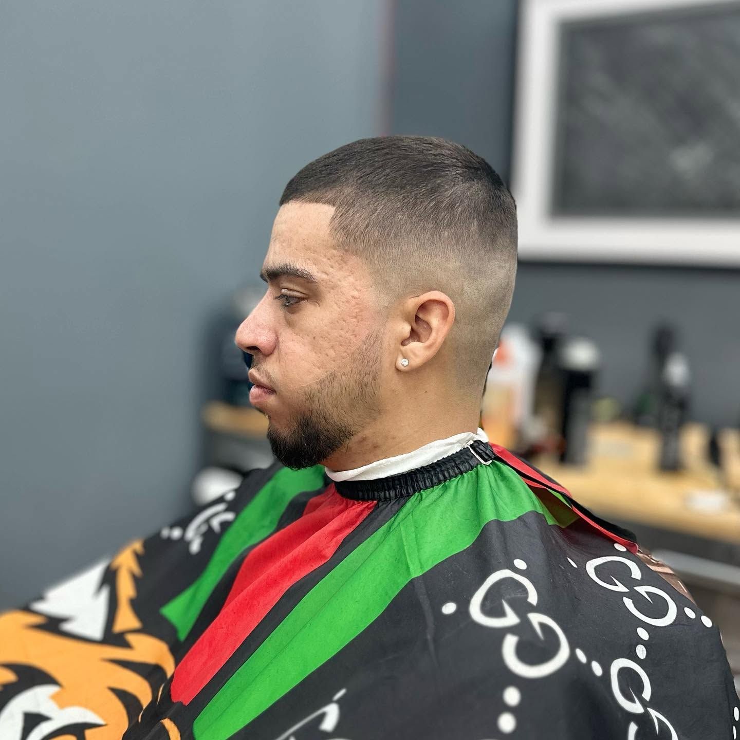 Man getting a fresh fade haircut in a barbershop, wearing a black cape with green and red stripes