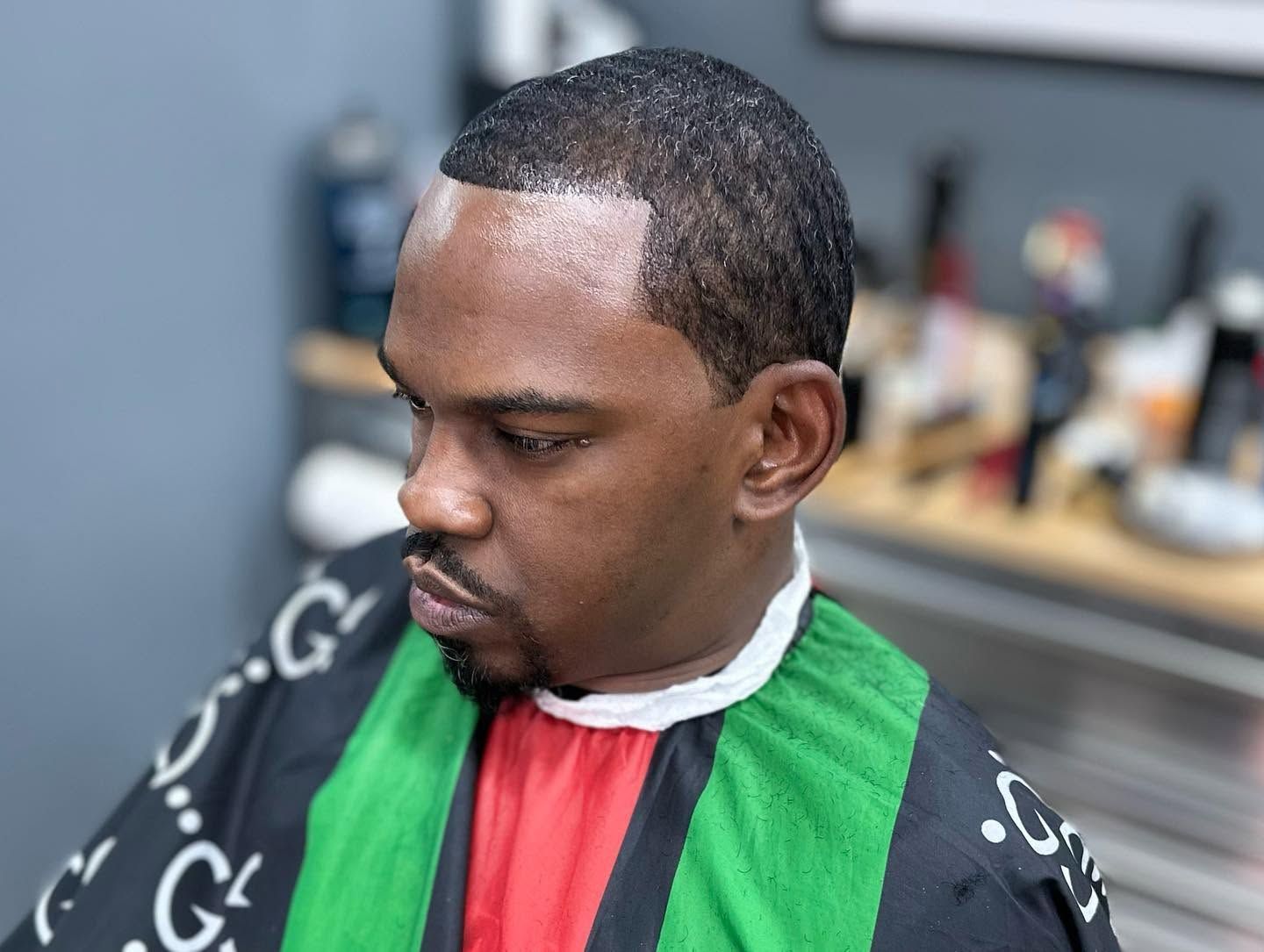 Close-up of a person in a black, green, and red barber cape, looking down in a salon chair.