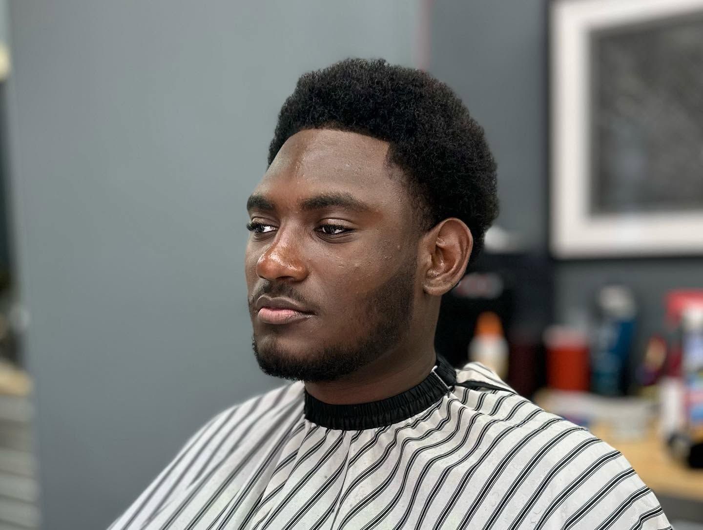 Person in a black-and-white striped barber cape, seated indoors with a neutral expression.