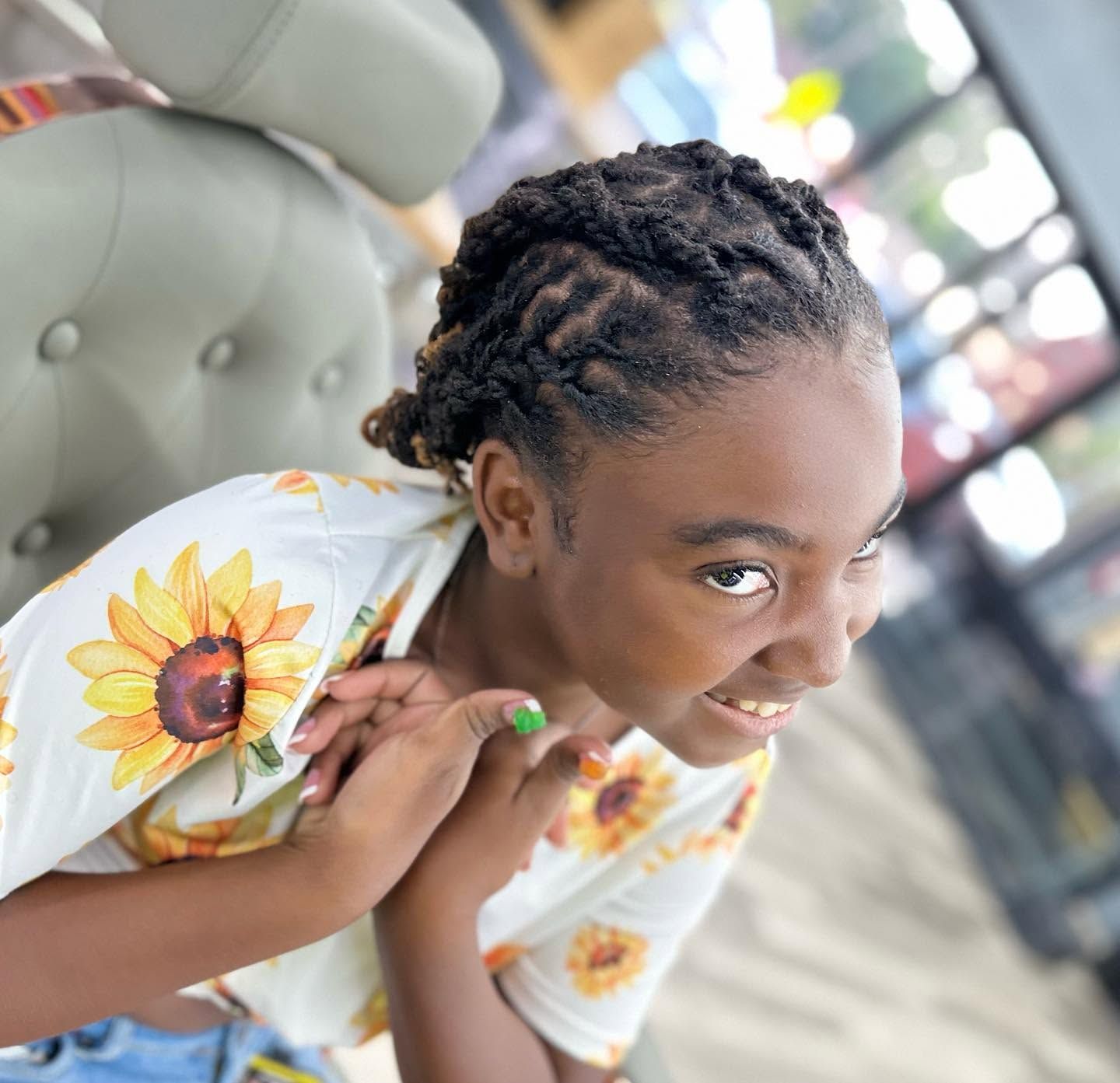 Smiling person in sunflower-print shirt leaning toward the camera outdoors on a bench