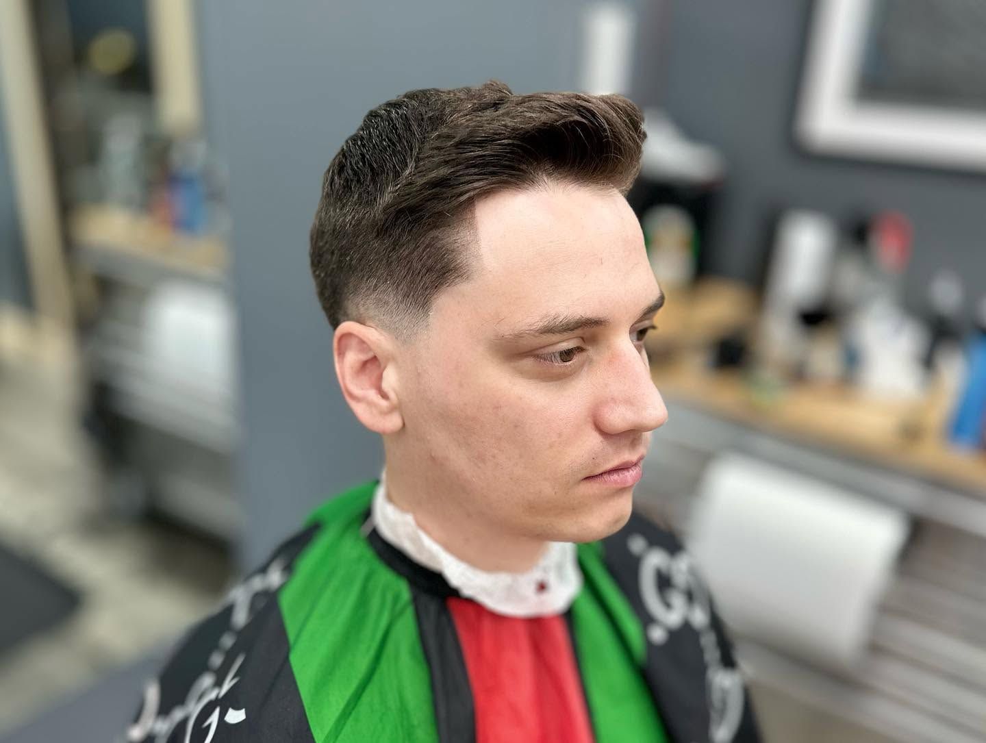 Person in a barber chair wearing a green, black, and red cape, with a fresh haircut in a salon.