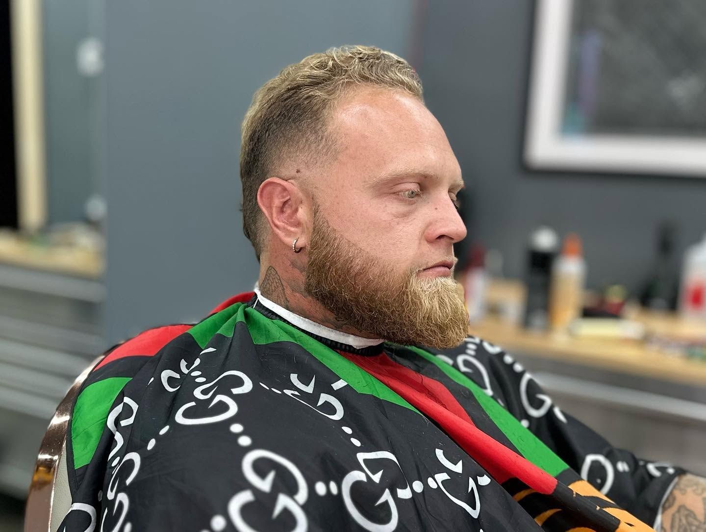 Man with a beard sitting in a salon chair wearing a black cape with green and red trim