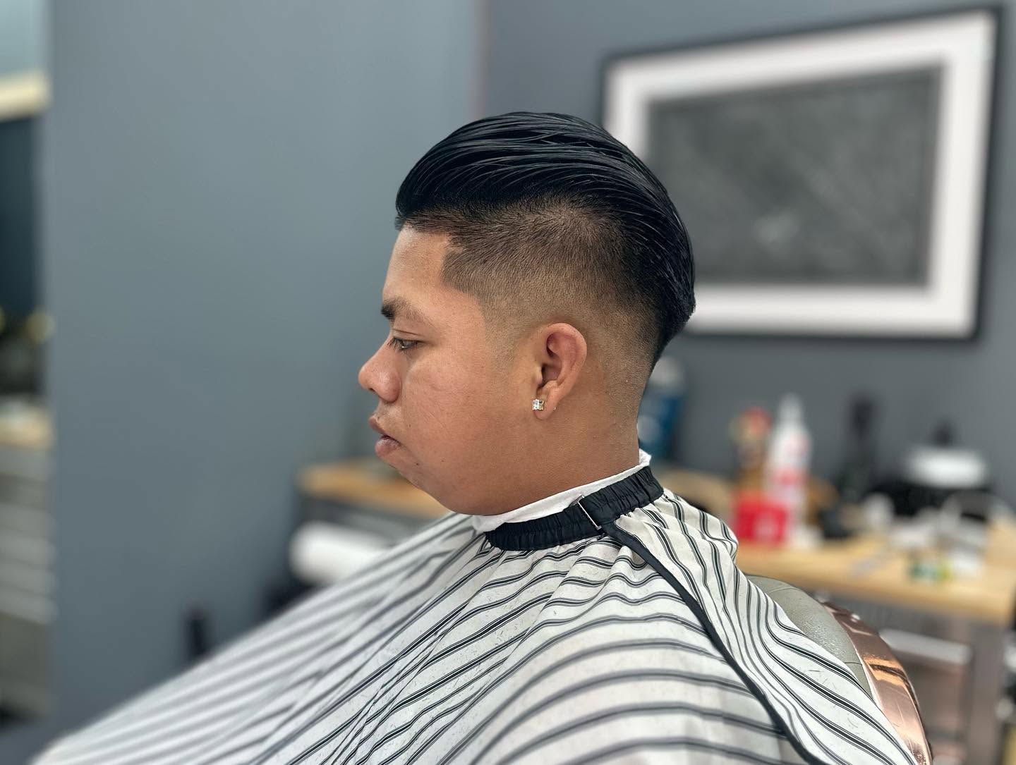 Man getting a haircut in a barbershop, wearing a striped cape, side profile visible
