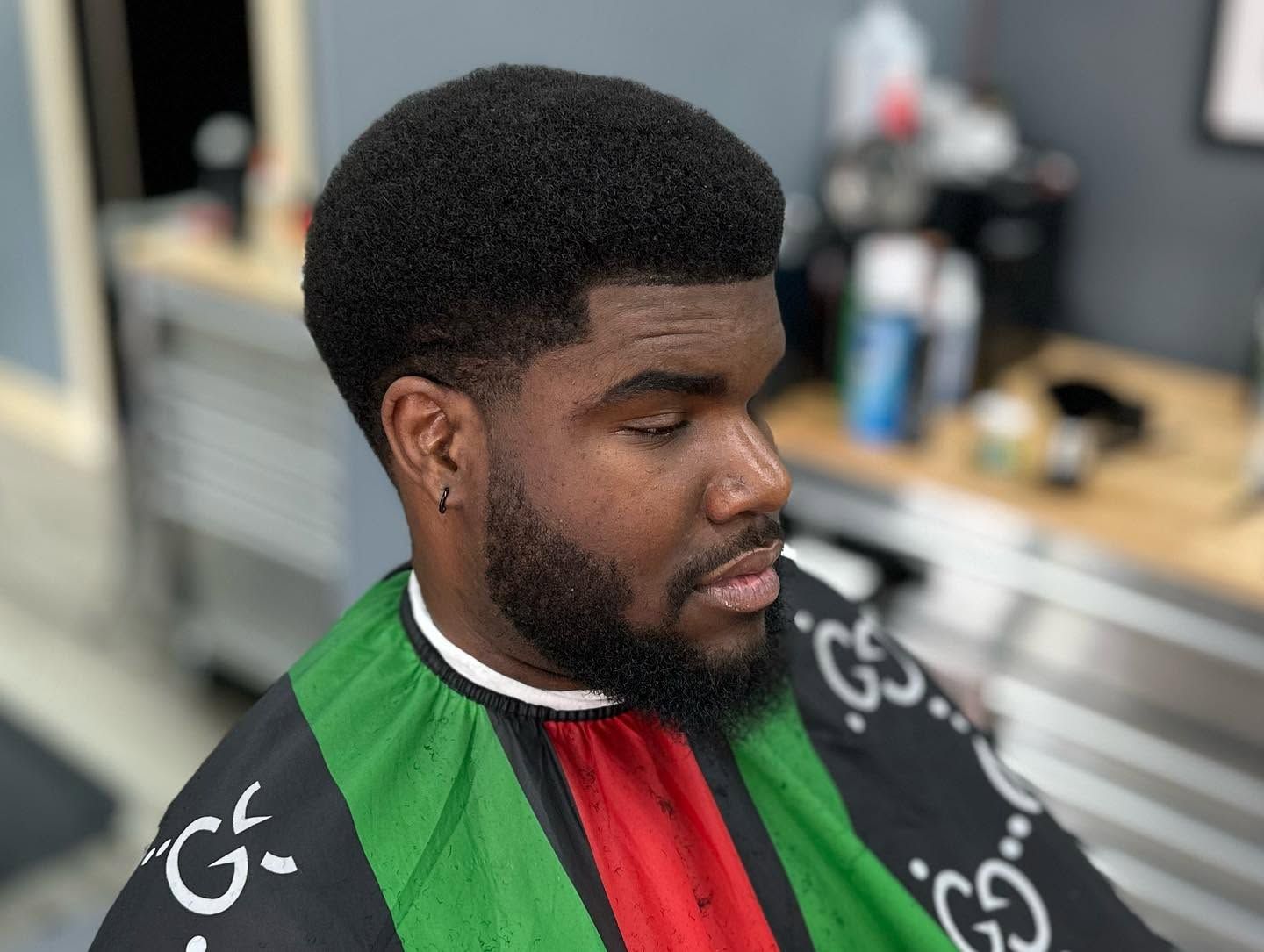 Man in a green, red, and black cape getting a haircut in a barbershop