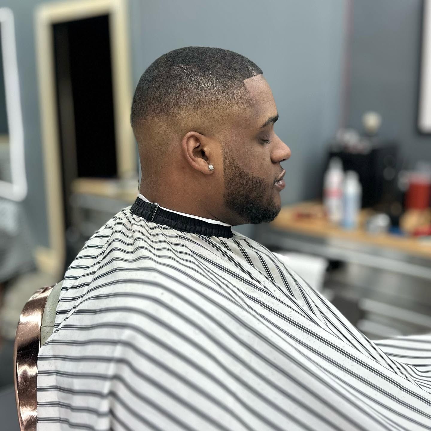 Man getting a short fade haircut in a barbershop, wearing a striped cape.