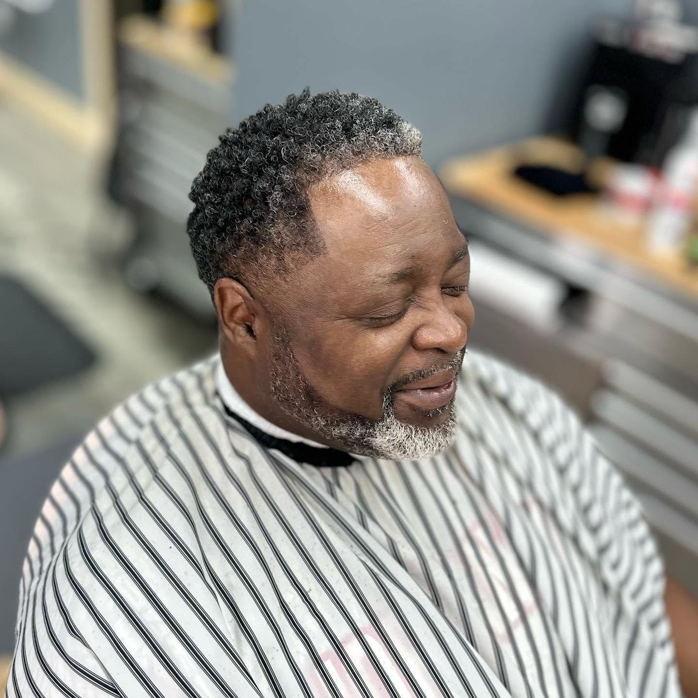 Man with eyes closed wearing a striped barber cape in a barbershop chair