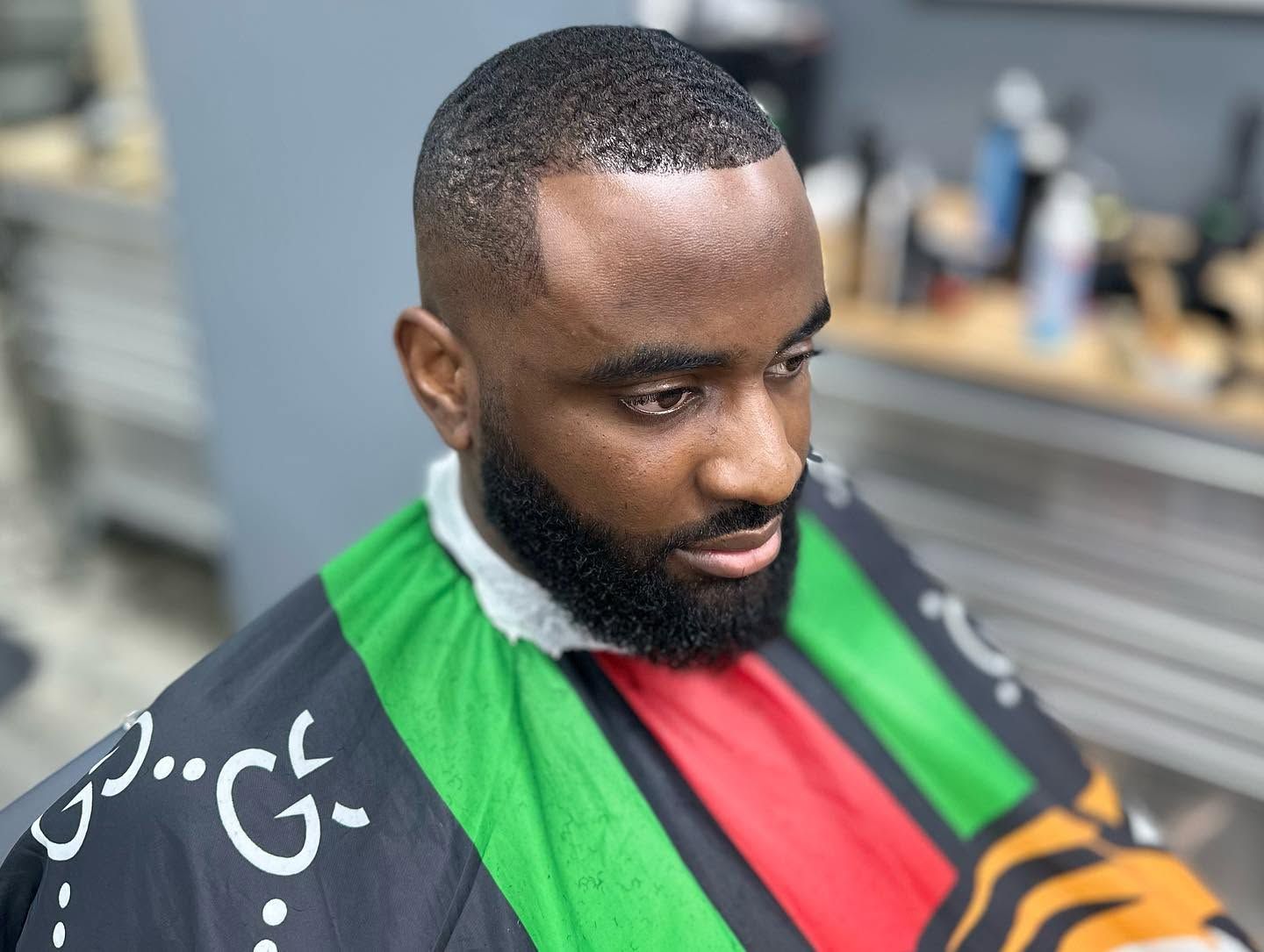 Man getting a haircut in a barbershop, wearing a black cape with bright green and red stripes.