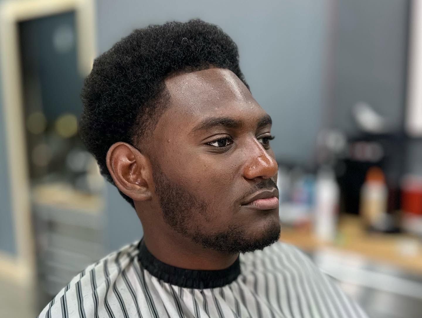 Man seated in a striped barber cape, looking to the side in a salon chair.
