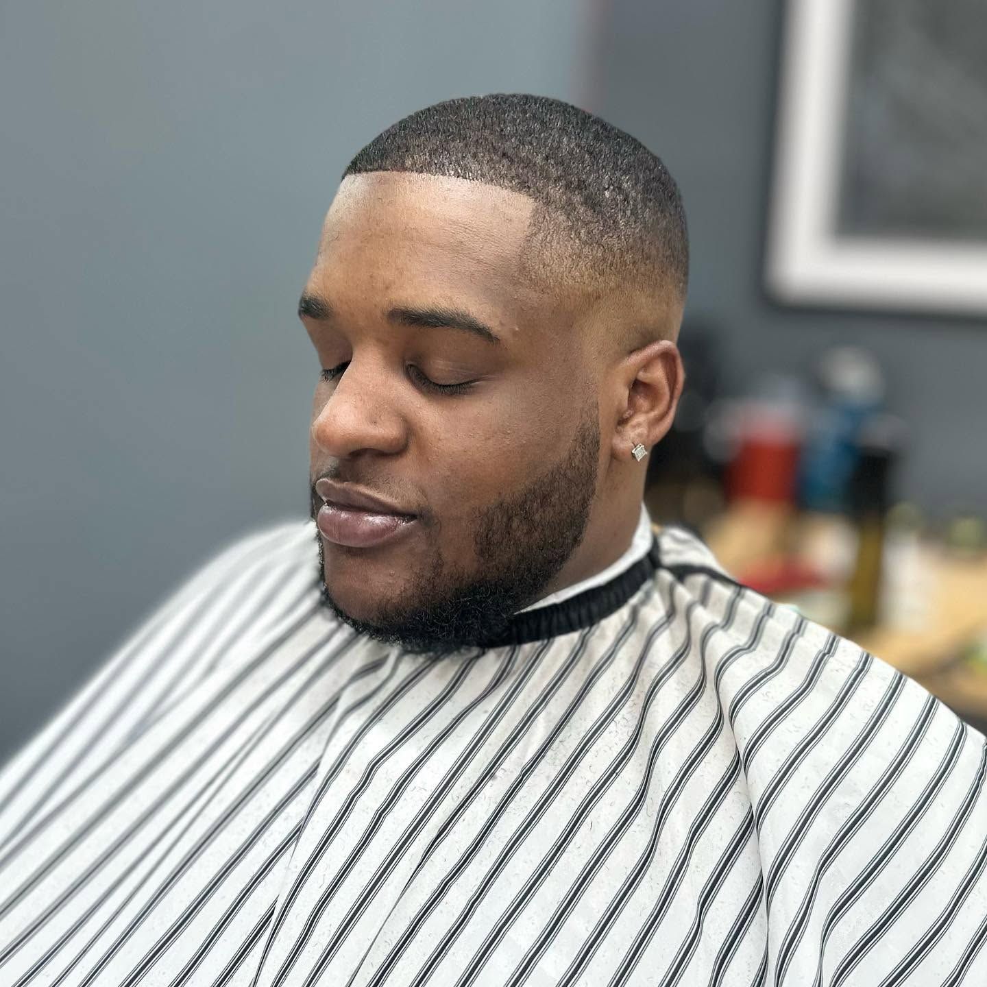 Man in a striped barber cape with a fresh fade haircut, seated in a barbershop chair.