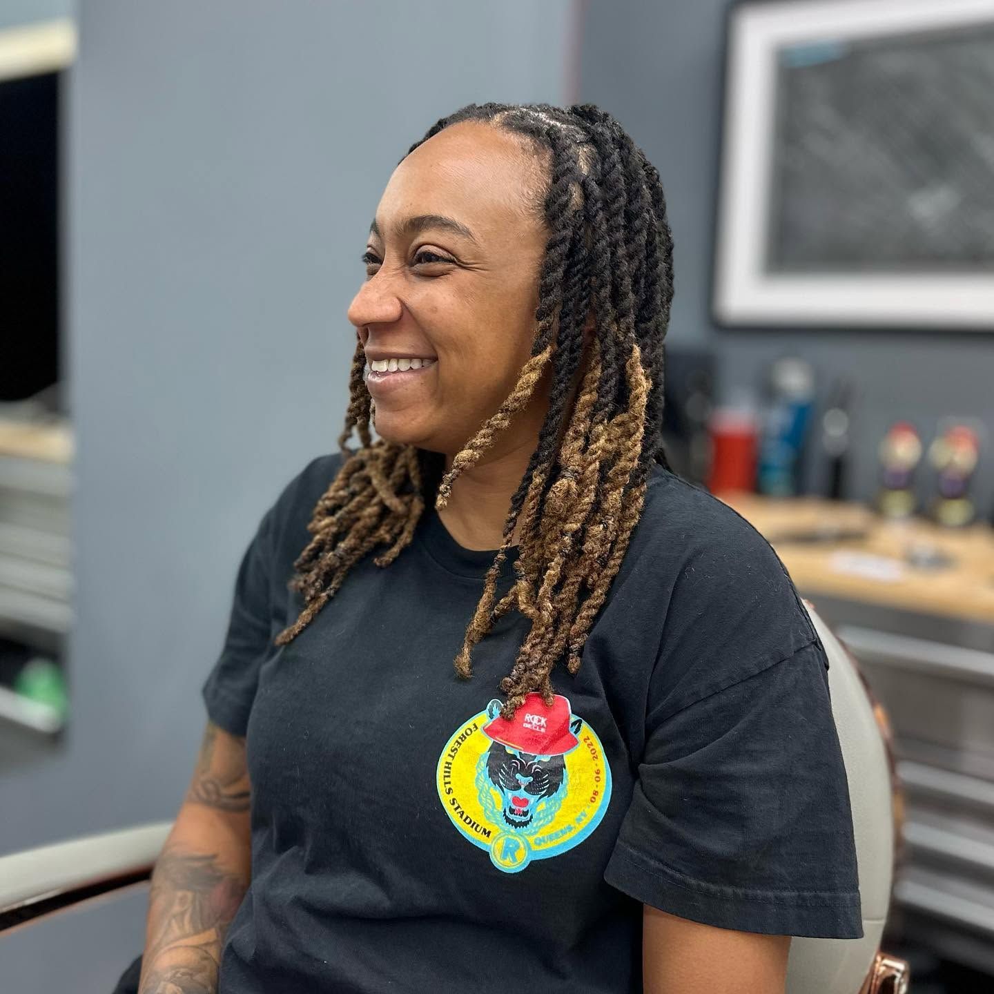 Smiling person with shoulder-length braids wearing a black T-shirt indoors