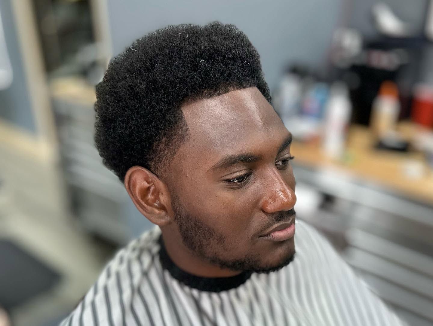 Portrait of a man with a high-top haircut in a striped barber cape, looking to the side in a barbershop.