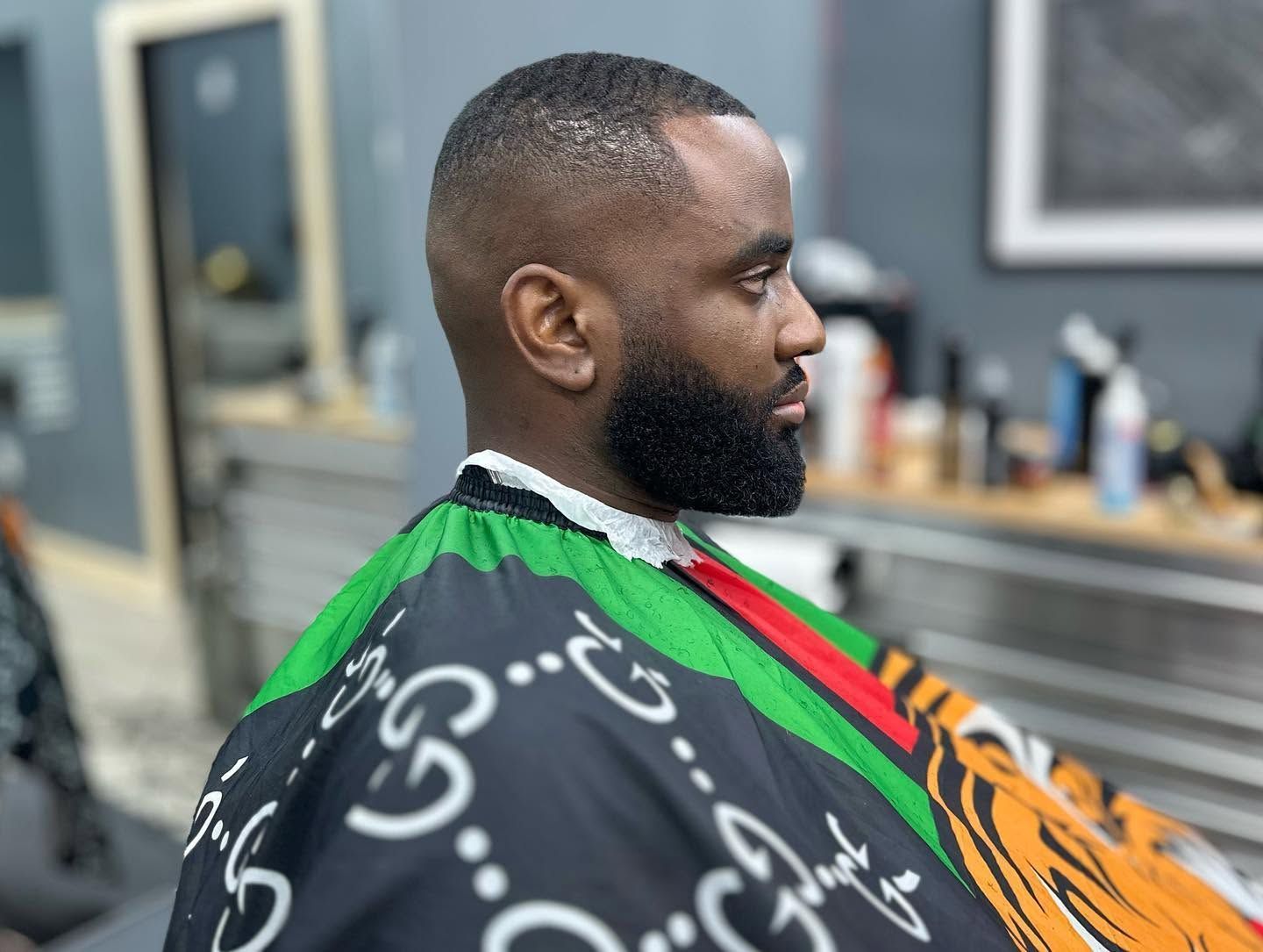 Man seated in a barber chair wearing a black cape with colorful patterns, getting a haircut in a salon.