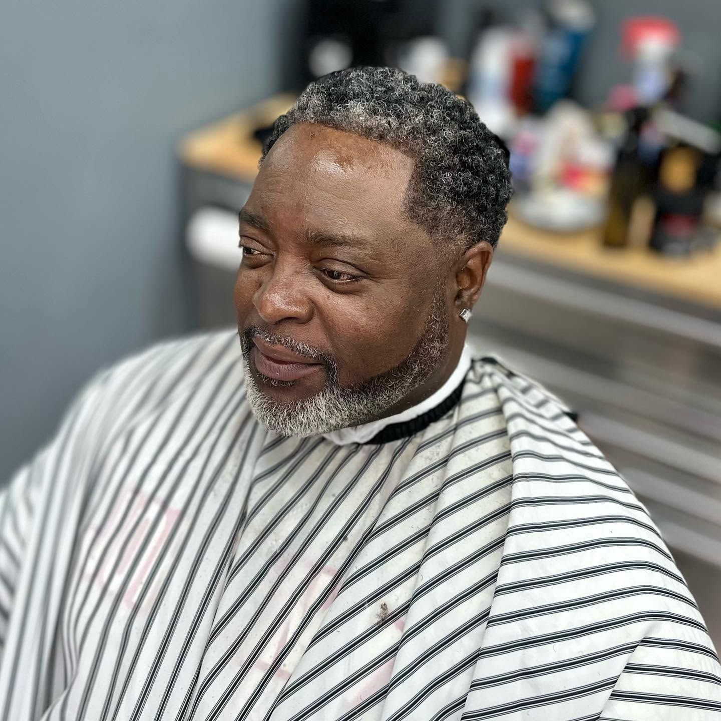 Man in a black-and-white striped barber cape, seated in a salon chair and looking to the side.