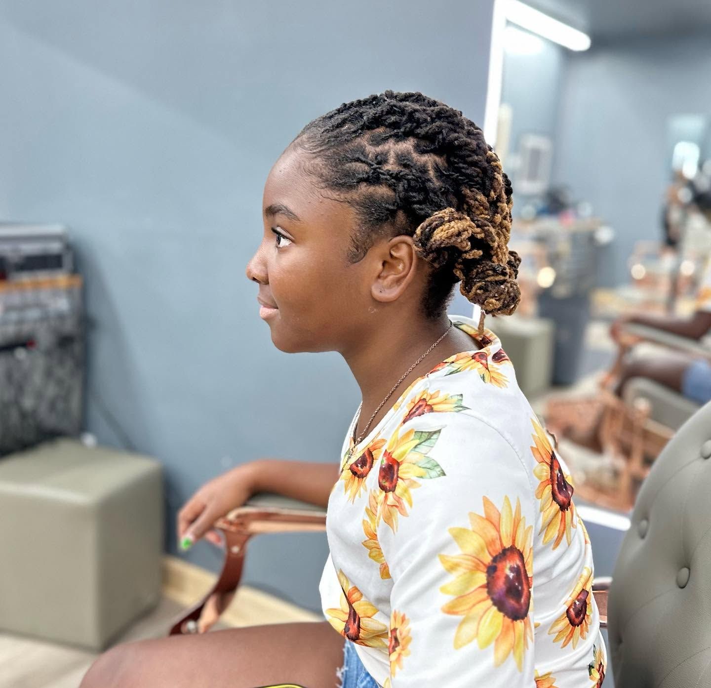 Profile of a child with braided hair in a sunflower shirt sitting in a salon chair
