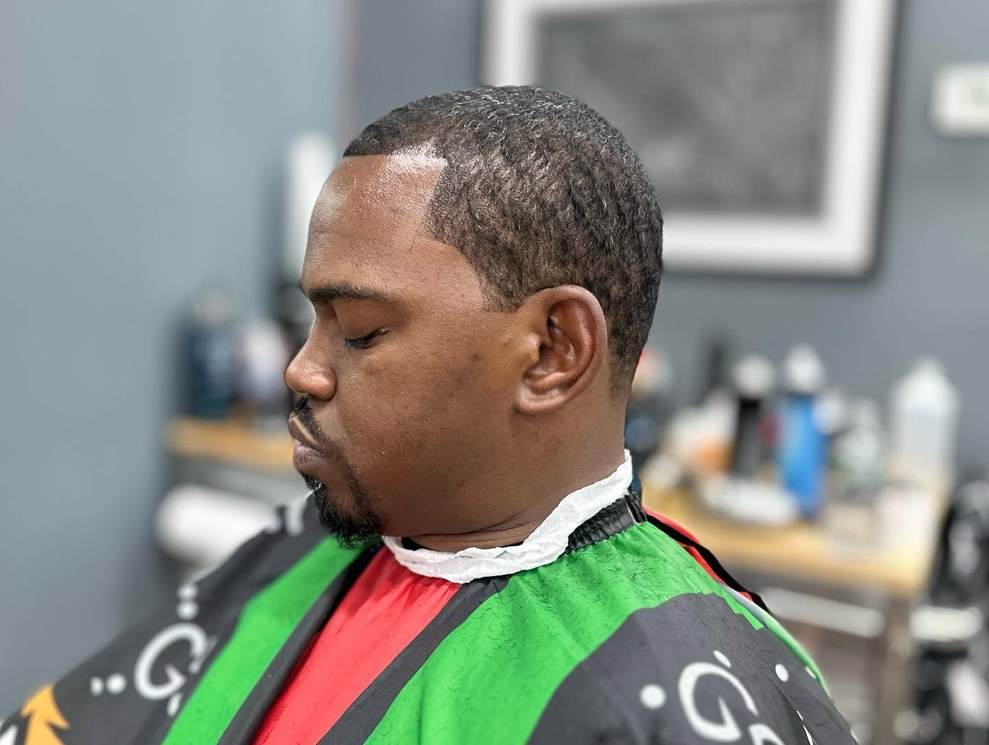 Close-up of a man getting a haircut, wearing a green barber cape in a salon